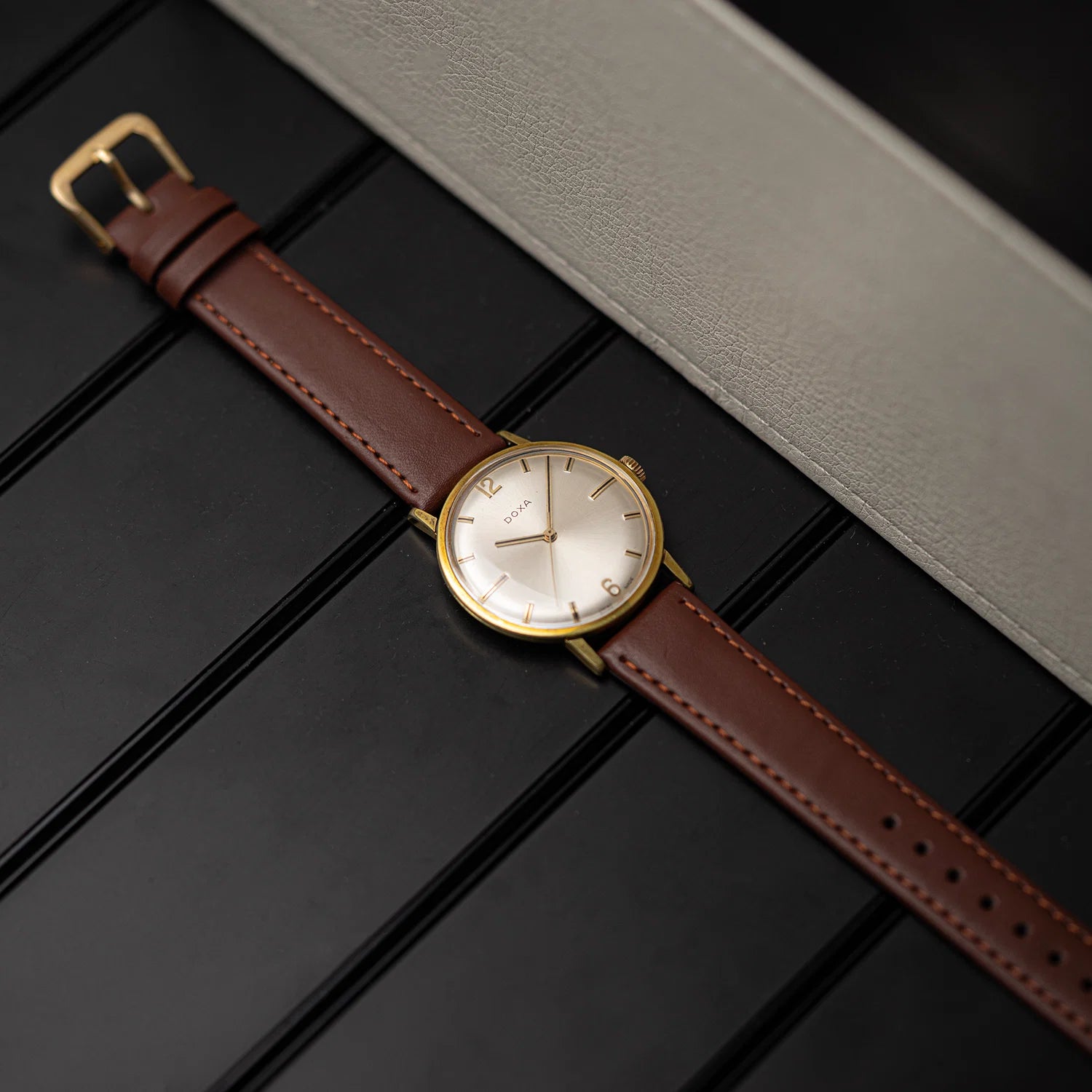 Doxa, Ref. 10346-5, Cal. 103, Men’s Manual Wind, 1970 with a brown leather strap and gold case on a dark surface