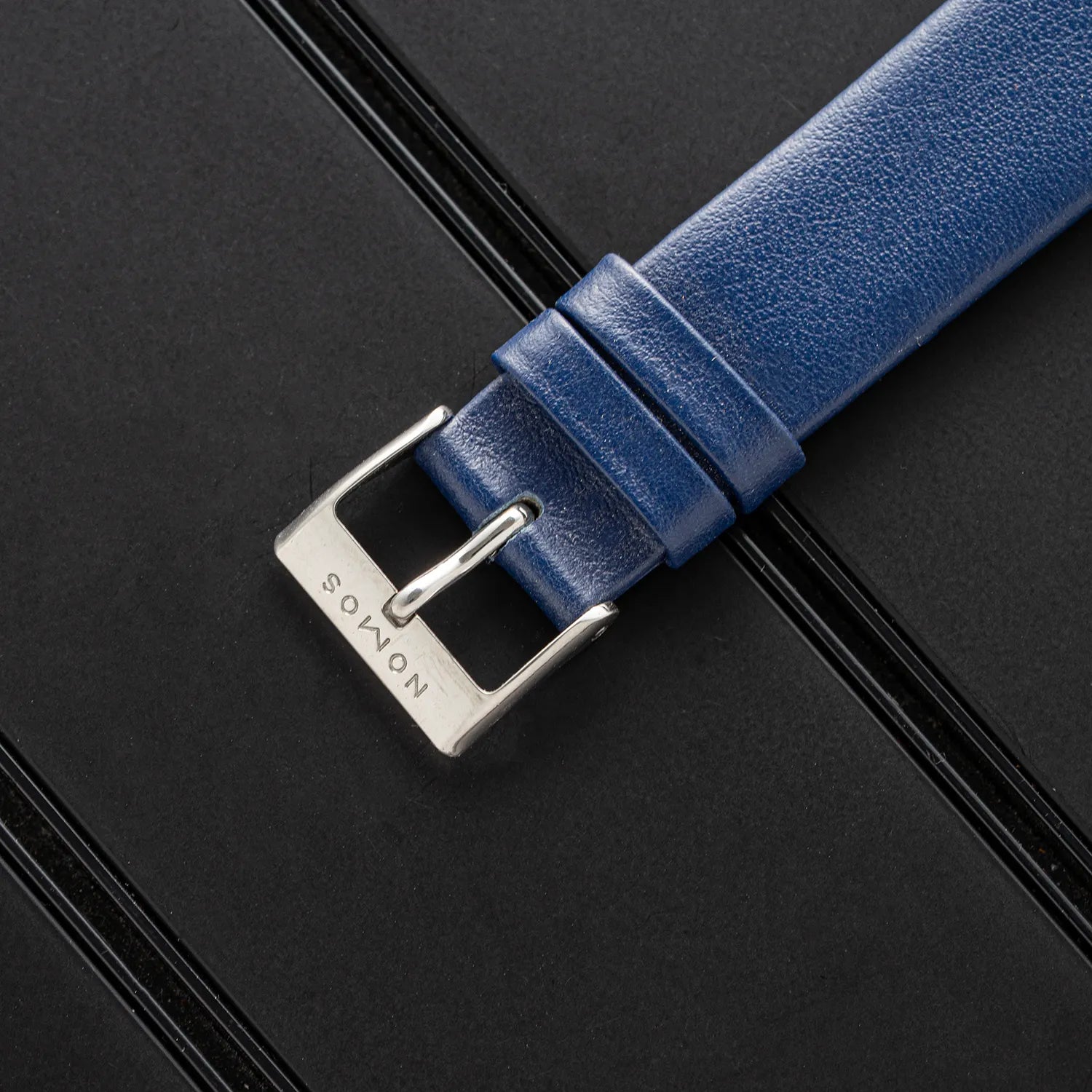 Blue leather watch strap with silver buckle on a black background