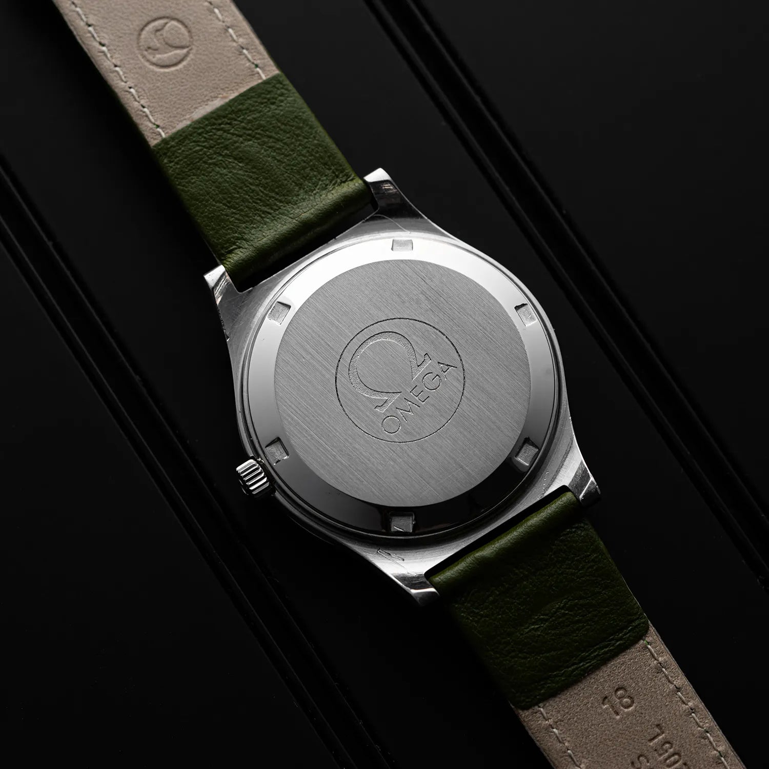 Close-up of a Omega Genève, Ref. 166.0168, Cal. 1012 Case back with a green strap on a black background