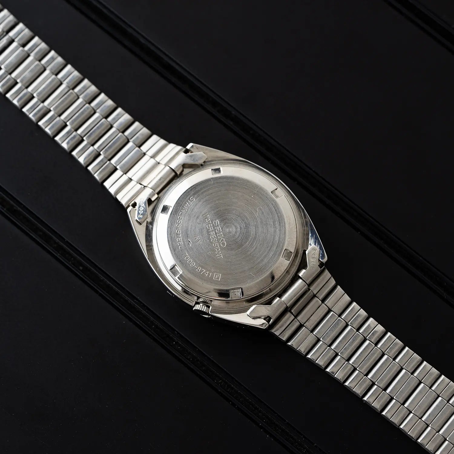 Seiko 5, Ref. 7009-8741 Caseback with metal strap on a black background