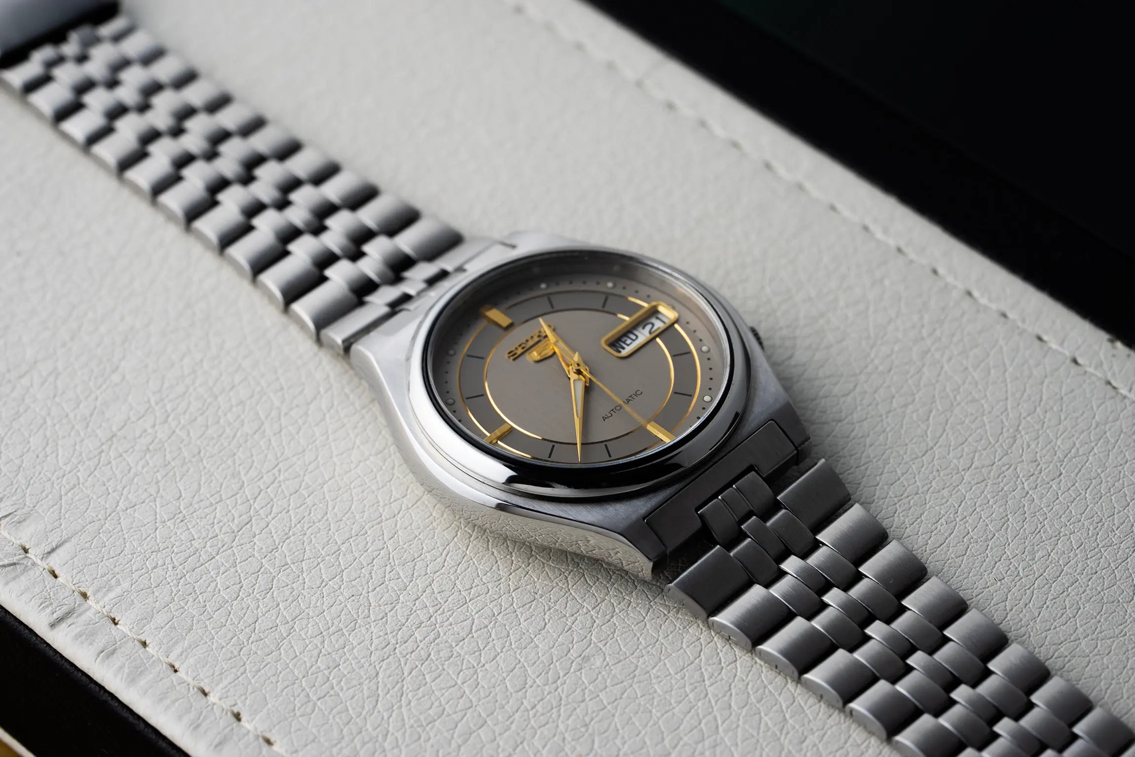 Silver Seiko 5 7S26 3170 case watch with a detailed face on a light gray surface
