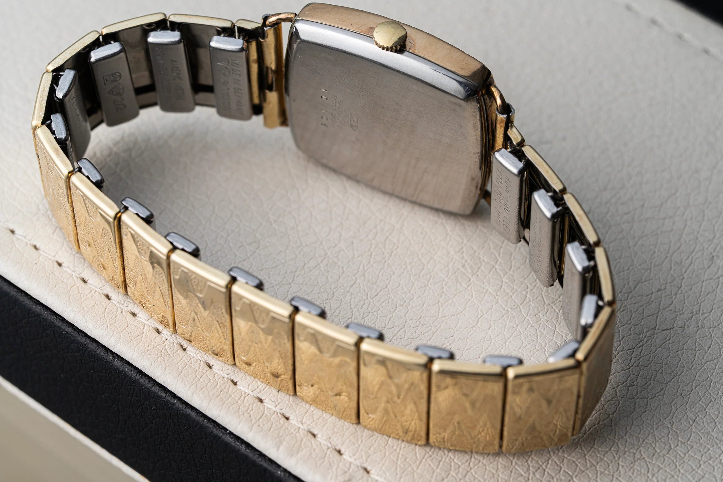 A close-up of a two-tone metal watch Bergana PUW 460 band, showing textured gold-tone links alternating with polished silver-tone links, resting on a light beige textured surface.