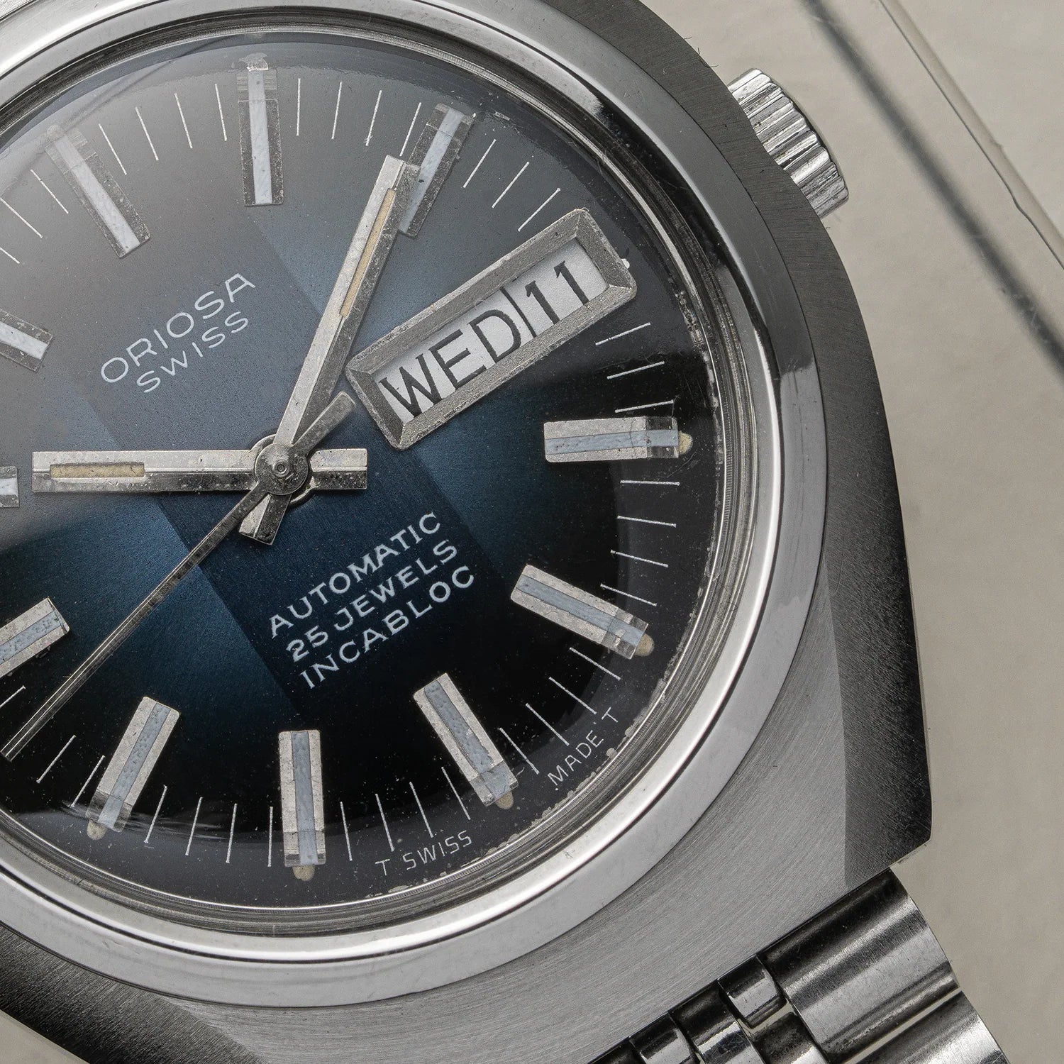 Close-up of an Oriosa Swiss Automatic 25 Jewels Incabloc watch with a dark blue sunburst dial, silver-tone case, and date window showing WED 11.