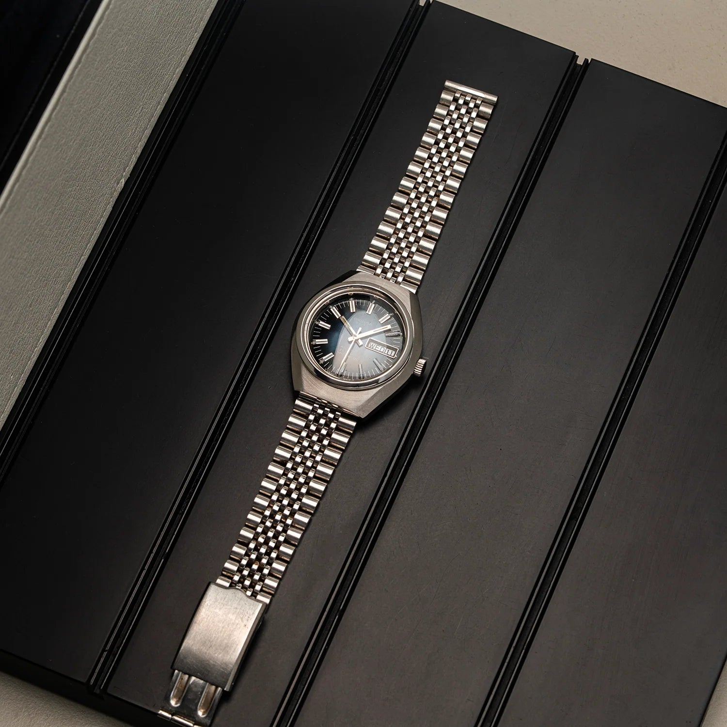 A vintage-style stainless steel wristwatch Oriosa, ETA 2789 with a textured metal link bracelet and a bluedial, displayed diagonally on a black presentation box.