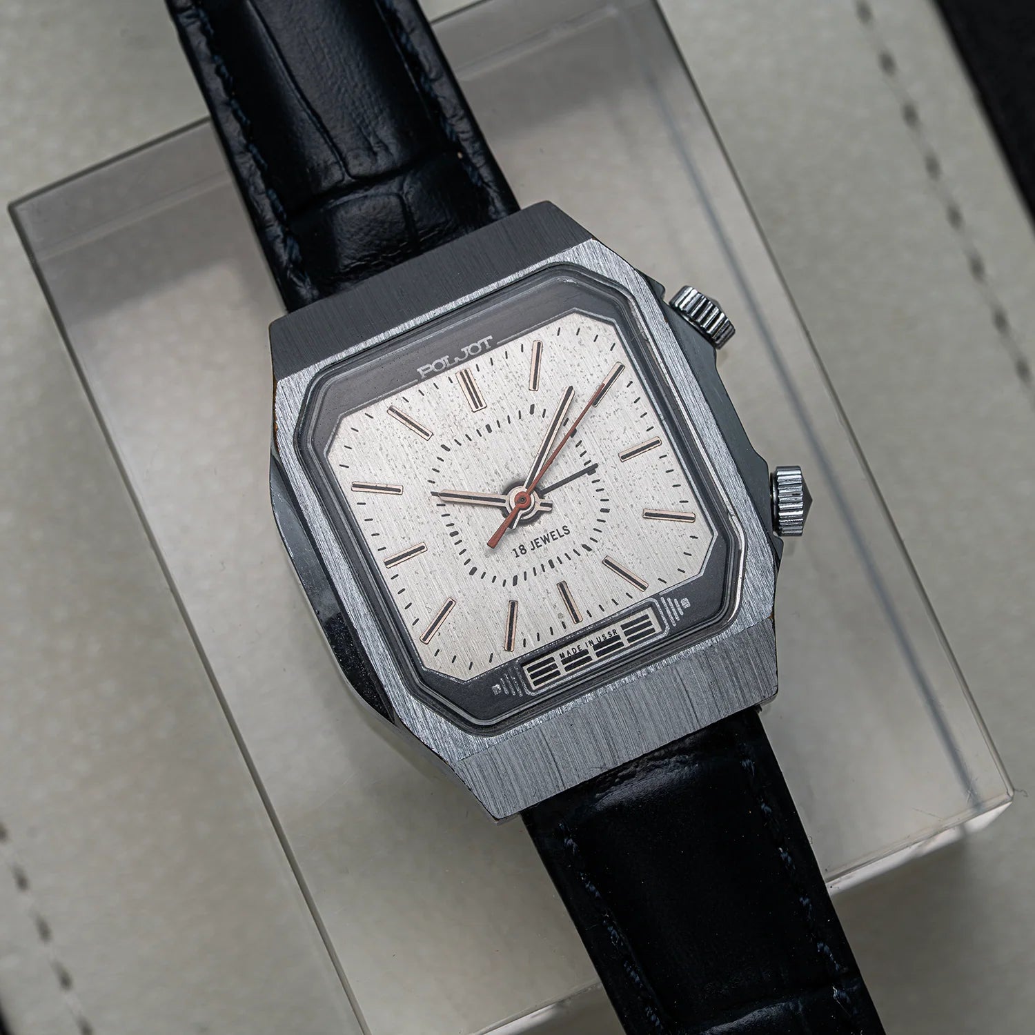 A wristwatch Poljot Alarm, Cal. 2612.1 with a brushed silver-tone metal case, a white textured dial, and a black leather strap, photographed at an angle on top of a light gray presentation box.