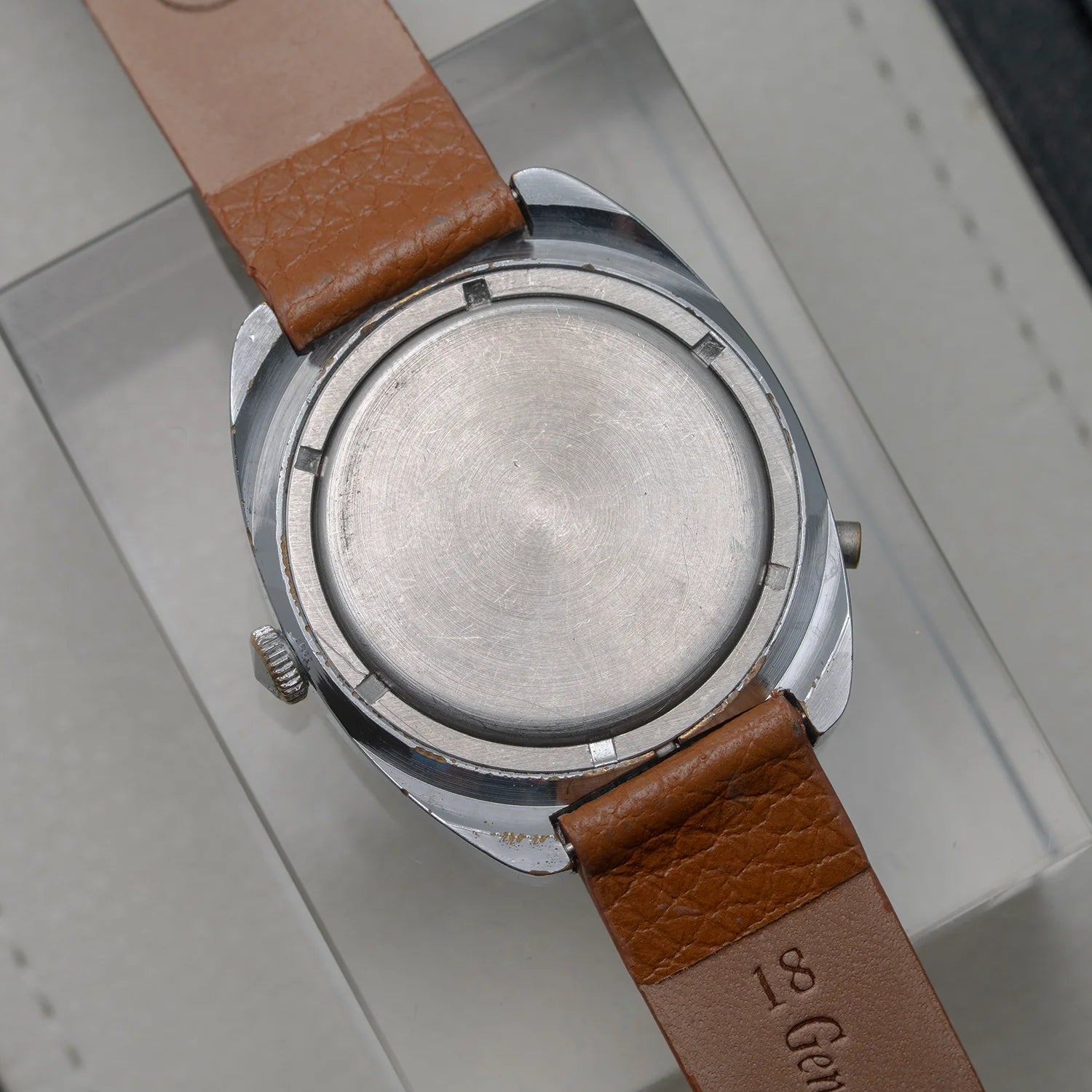Close-up of the back of a vintage wristwatch Poljot with a silver-tone metal case and a brown leather strap, resting on a light gray display surface.