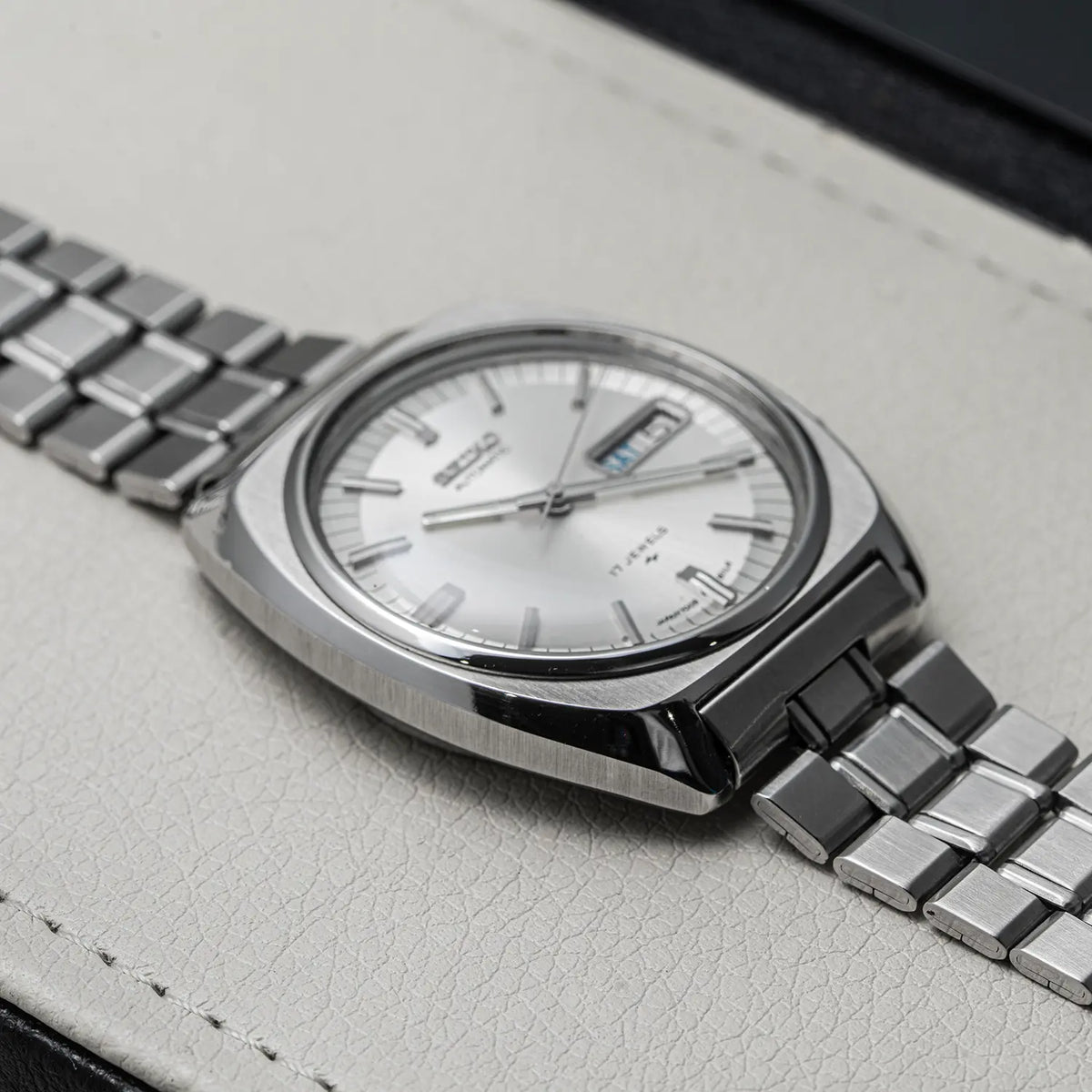 A close-up of a Seiko, Ref. 7009-8100, Cal. 7009, Men’s Automatic, 1977 watch with a silver-toned stainless steel case, silver dial, and matching steel link bracelet, resting on a light textured surface.