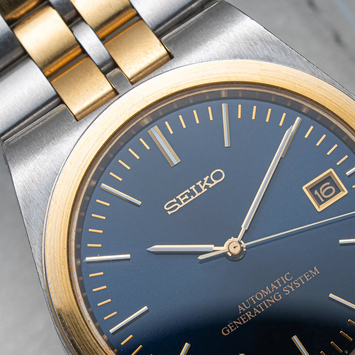 Close-up of a Seiko AGS, Ref. 5M22-8A10, Cal. 5M22, Men’s Quartz Analog watch with a blue dial, gold-tone bezel and hands, and a two-tone stainless steel and gold-tone bracelet.