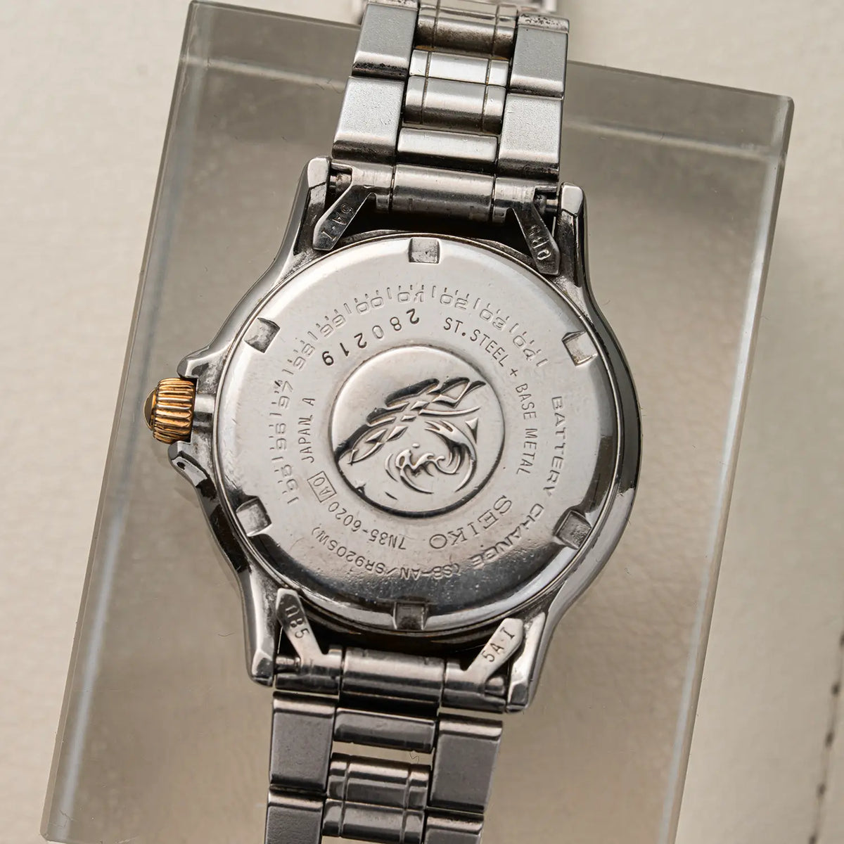 Close-up of the back of a silver-tone Seiko Scuba 200M, Ref. 7N35-6020, Cal. 7N35, Diving, 1992 wristwatch with a metal link bracelet and a gold-tone crown, mounted on a clear display stand.