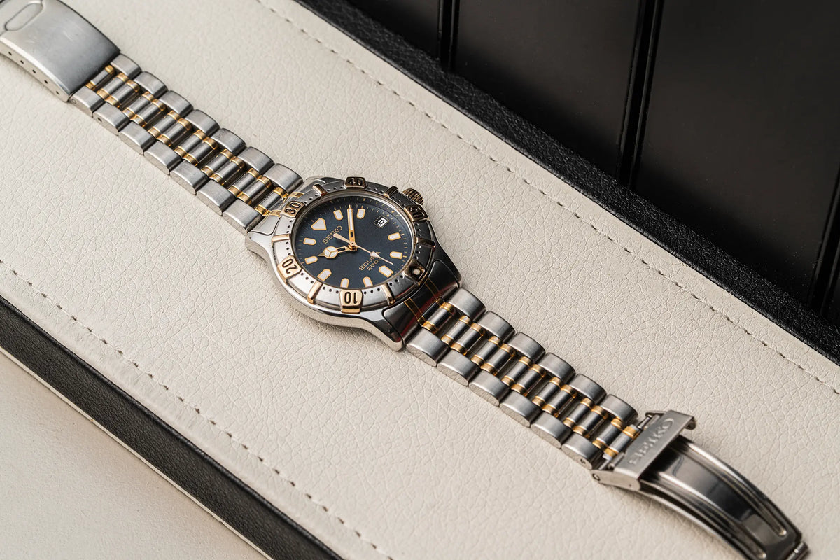 A lSeiko Scuba 200M, Ref. 7N35-6020, Cal. 7N35, Diving, 1992wristwatch with a silver and gold-tone metal link bracelet, a stainless steel bezel, and a dark blue dial, resting on a cream-colored leather surface.