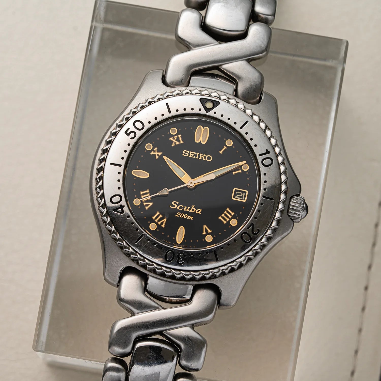 A Seiko Scuba watch with a silver-toned metal link bracelet and a black dial, displayed on a clear acrylic stand.