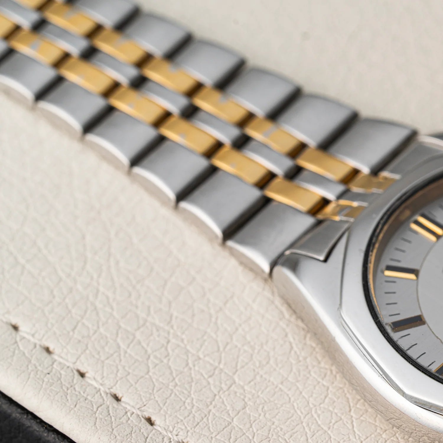 Close-up of a two-tone stainless steel and gold watch Seiko SQ 5Y23-8240 band with a silver-toned watch case and dial, resting on a textured off-white leather surface.