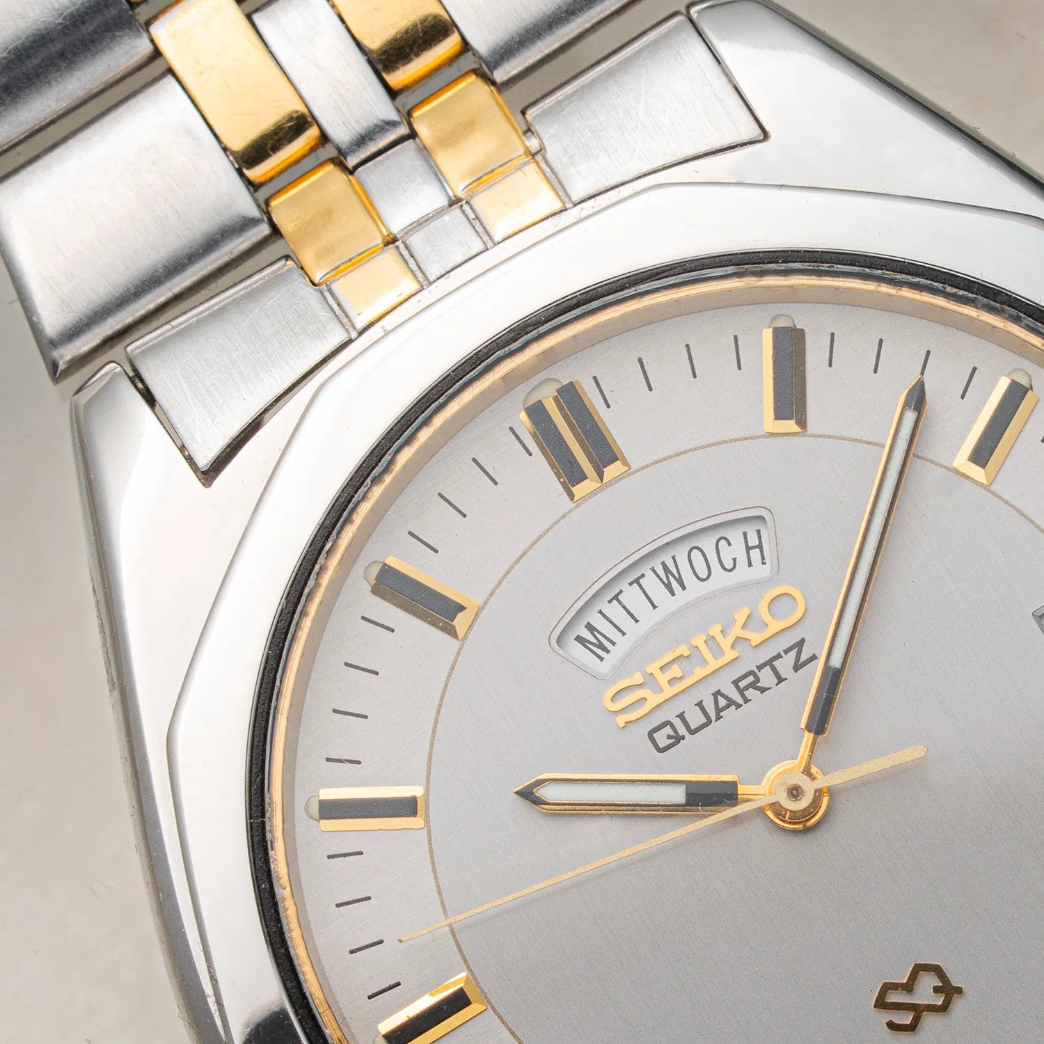 Close-up of a Seiko SQ 5Y23-8240 watch with a silver-toned stainless steel case, gold-toned accents on the dial and bracelet, and a silver dial with black hour markers.