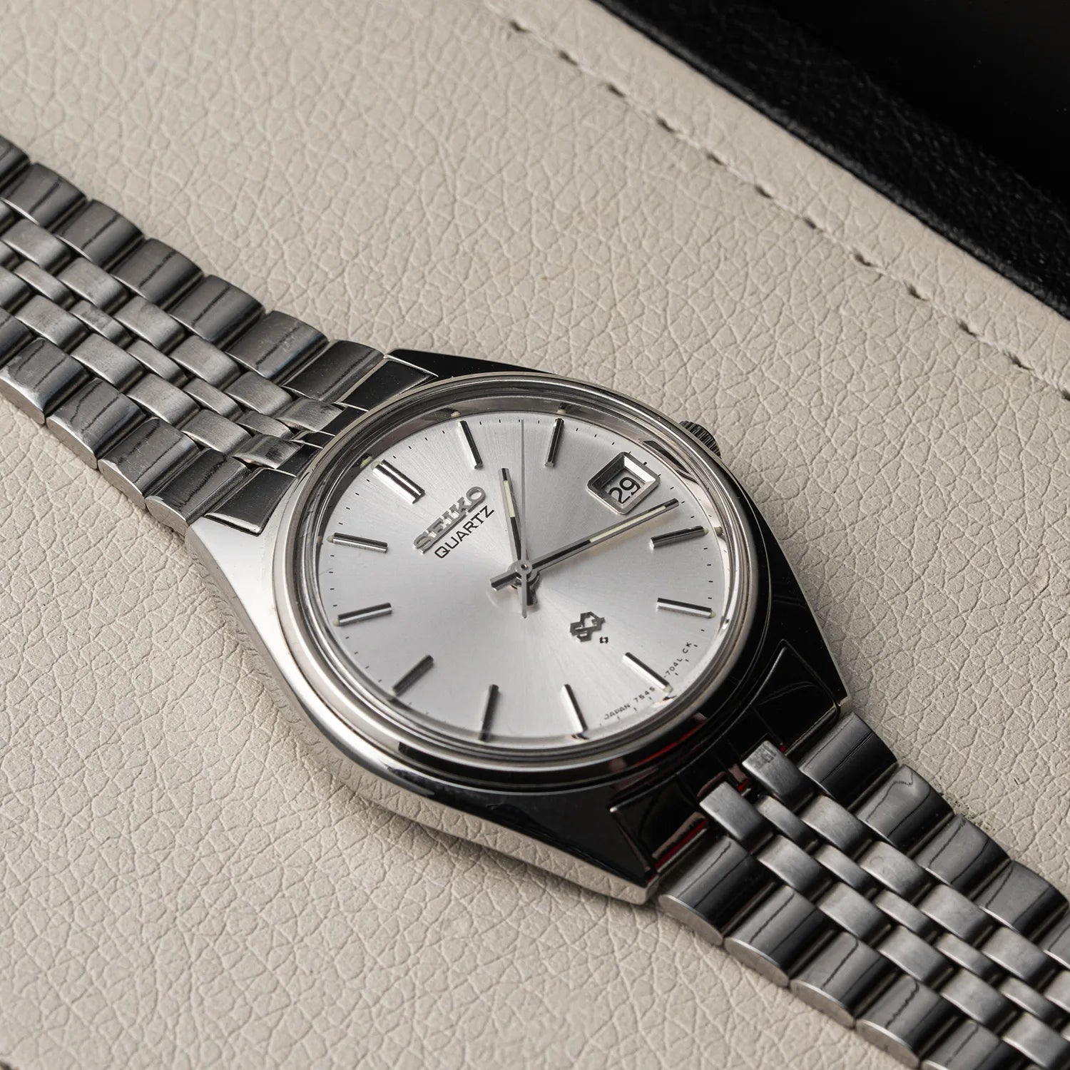 A Seiko SQ, Ref. 7545-7030 watch with a silver dial and stainless steel link bracelet, resting on a textured light beige leather surface.
