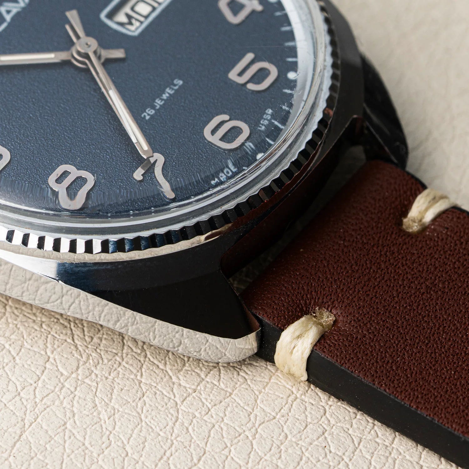 Close-up of a wristwatch Slava Big Numerals with a dark blue dial, silver-tone numerals and hands, a black case, and a brown leather strap with white stitching, resting on a textured beige surface.