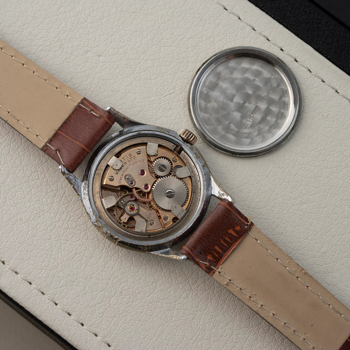 Watch Fortis, Ref. 2127, Cal. ETA 1080, Men’s Manual Wind, 1958 with brown leather strap and visible mechanical components on a beige surface