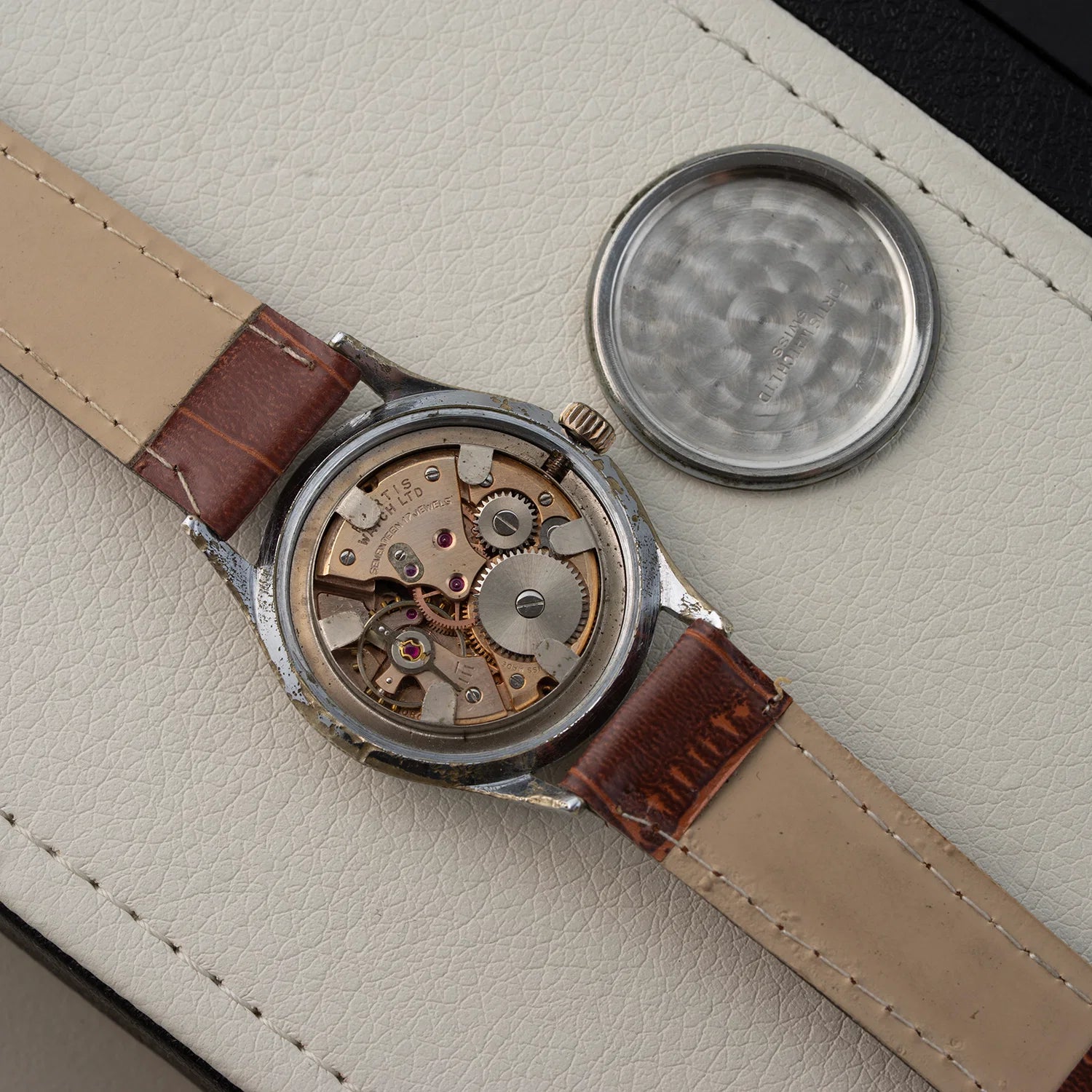 Watch Fortis, Ref. 2127, Cal. ETA 1080, Men’s Manual Wind, 1958 with brown leather strap and visible mechanical components on a beige surface
