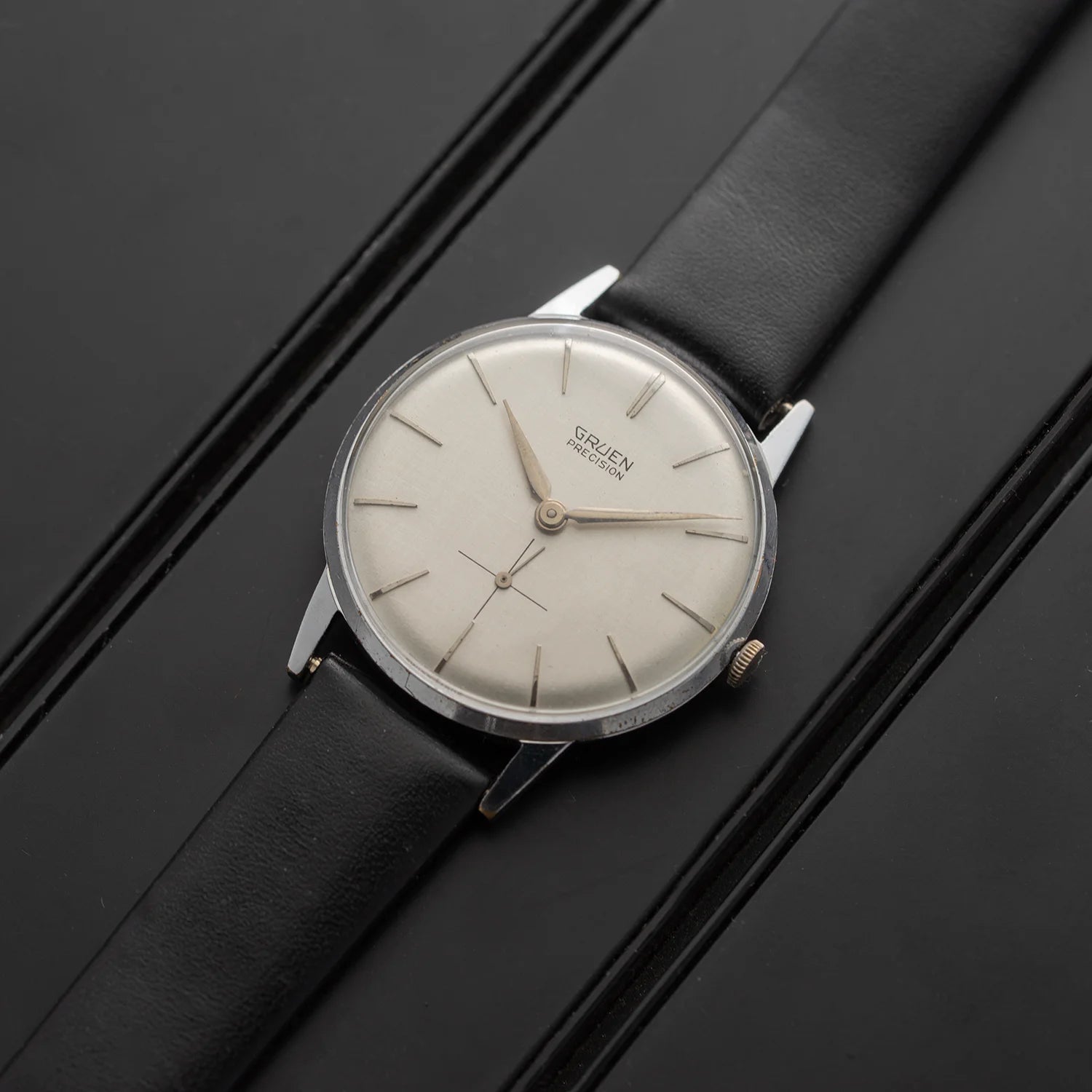 Gruen Precision vintage men’s watch with silver dial, small seconds, and black leather strap, angled front view