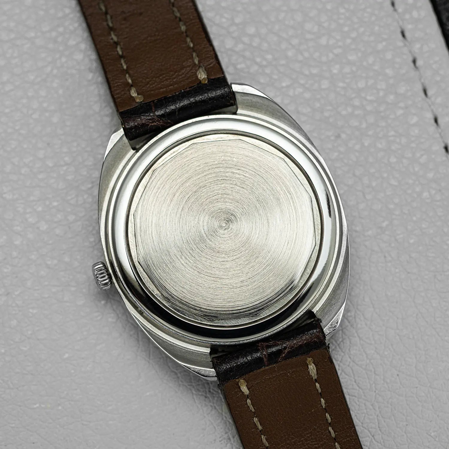 Close-up of a Longines Conquest Ref 1500 Cal 706 backcase with a brown leather strap on a gray textured background