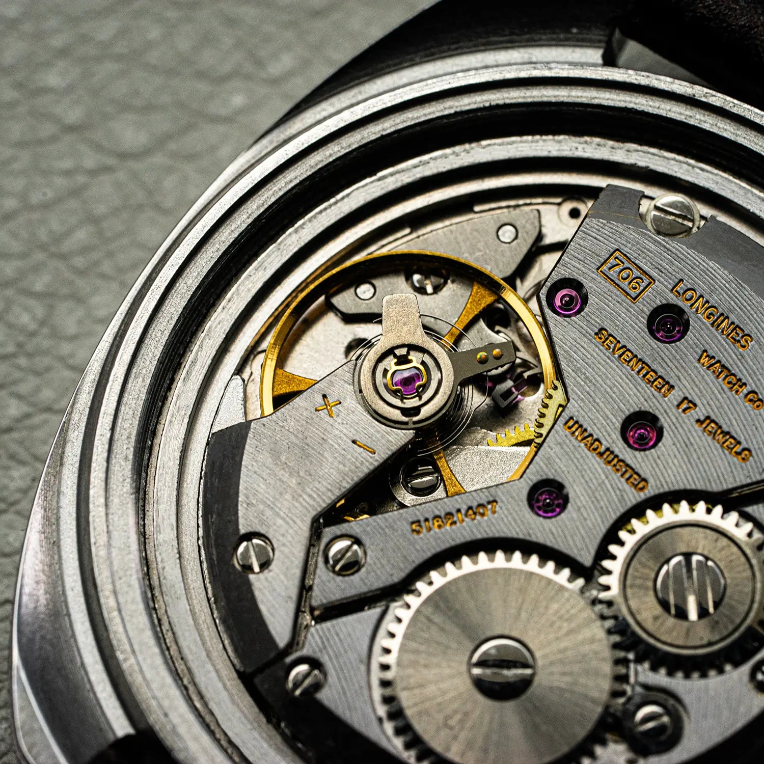 Close-up of a Longines Conquest Ref 1500 Cal 706 watch mechanism with visible brand name on a textured gray background