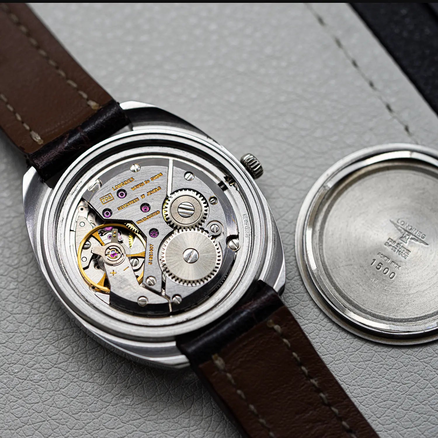 Watch with brown leather strap and visible mechanical components on a gray textured surface