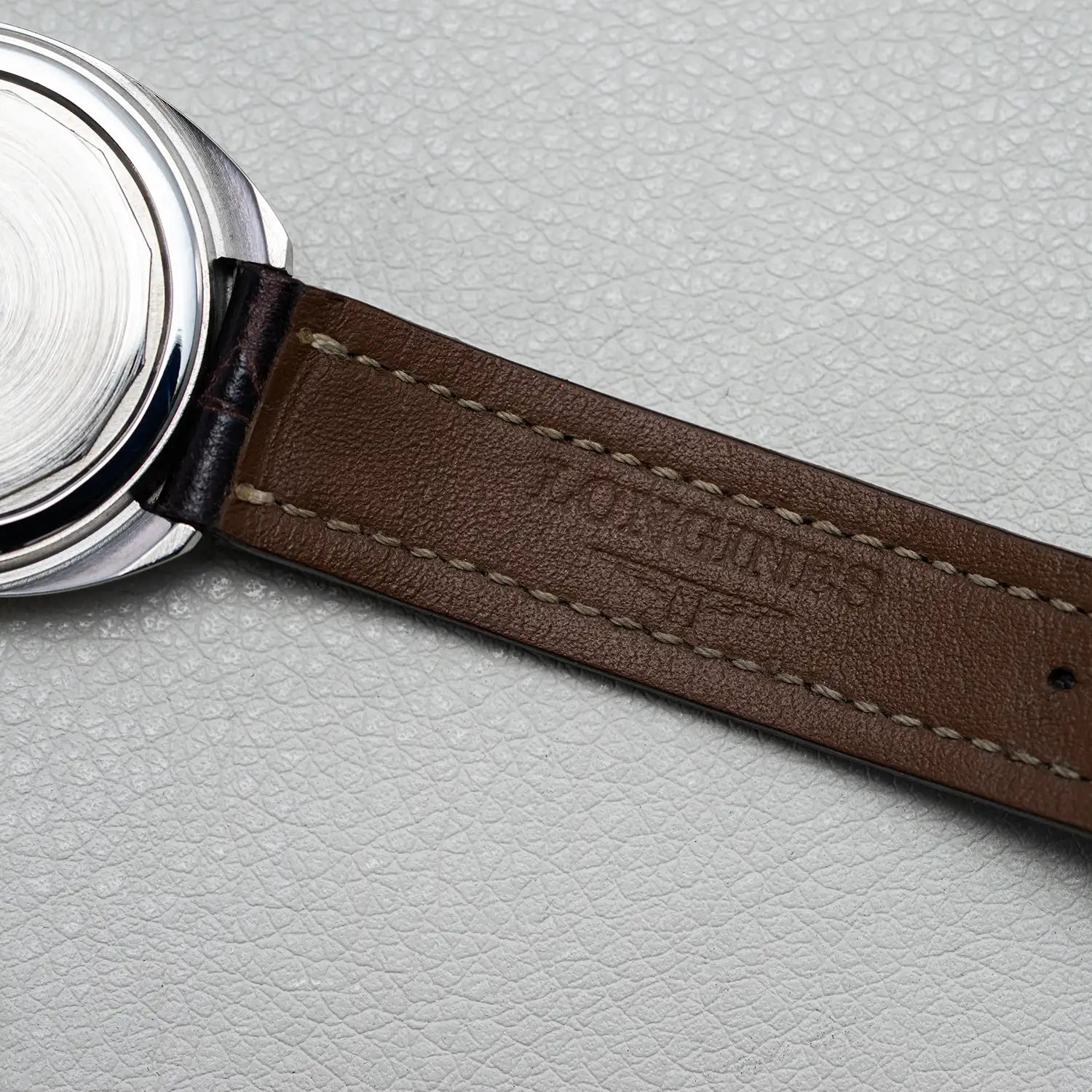 Close-up of a Longines Conquest Ref 1500 Cal 706 watch with a brown leather strap on a light gray background