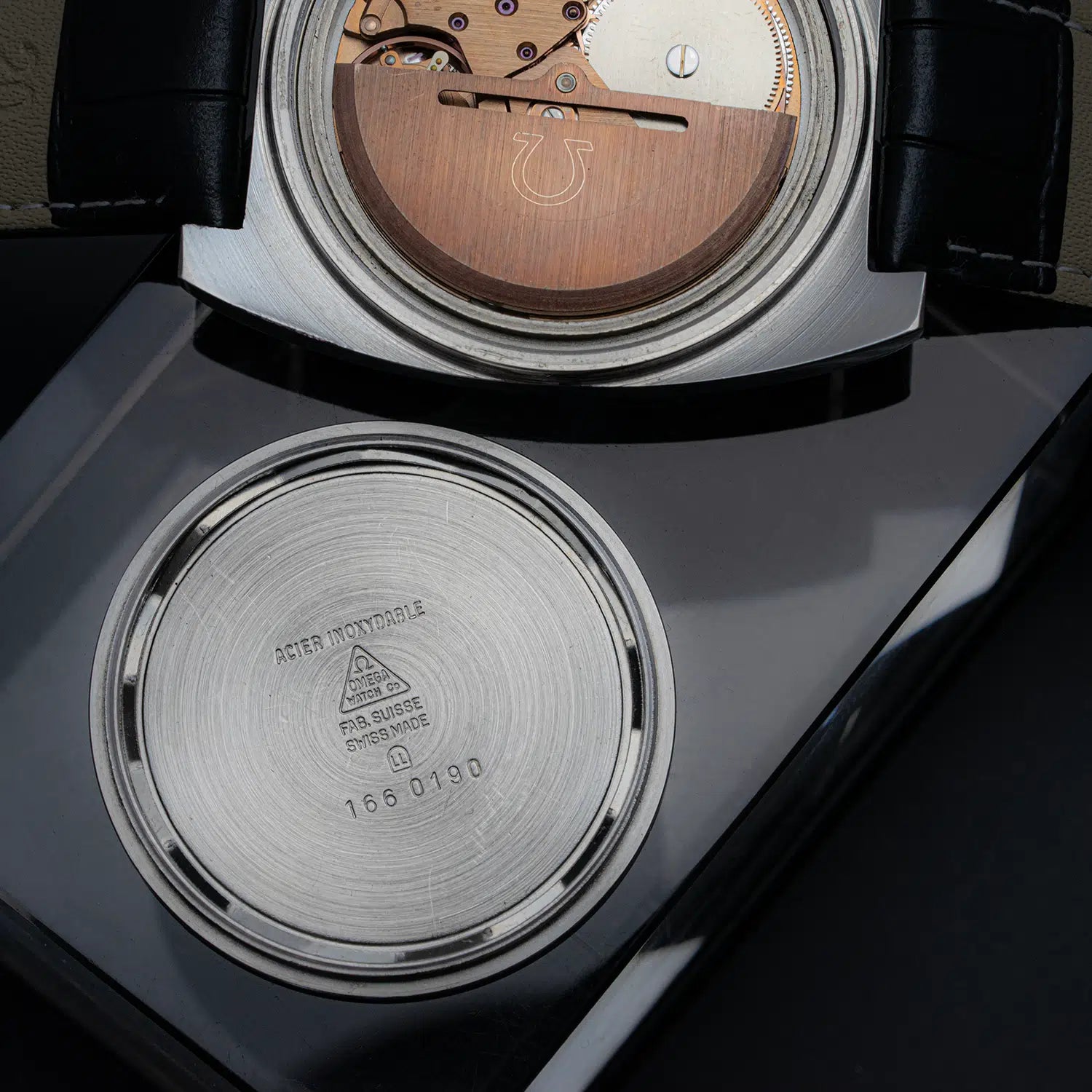 Close-up of a watch with its back cover open showing reference 166.0190 , revealing the mechanical components