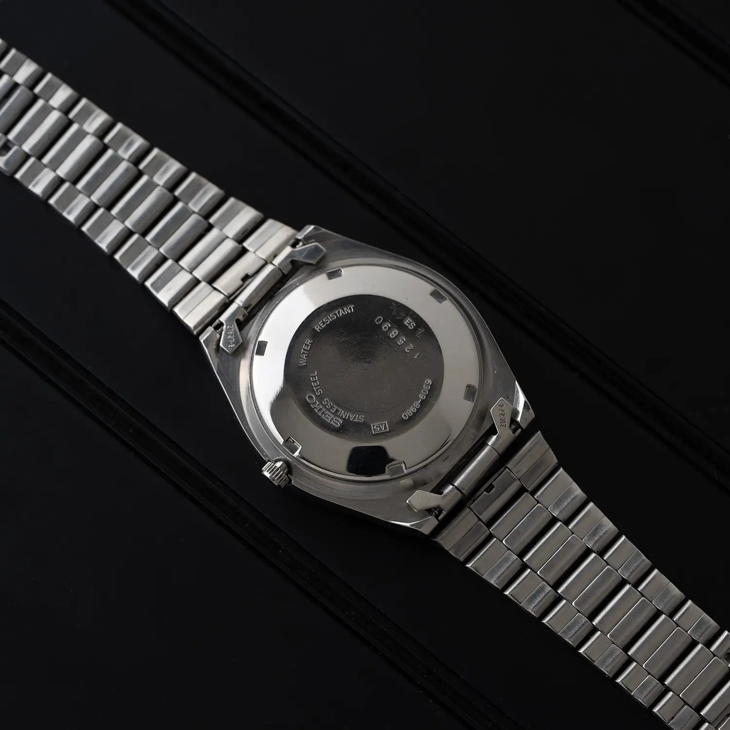 Seiko 5 6309 8980 case back with a metallic band on a black background