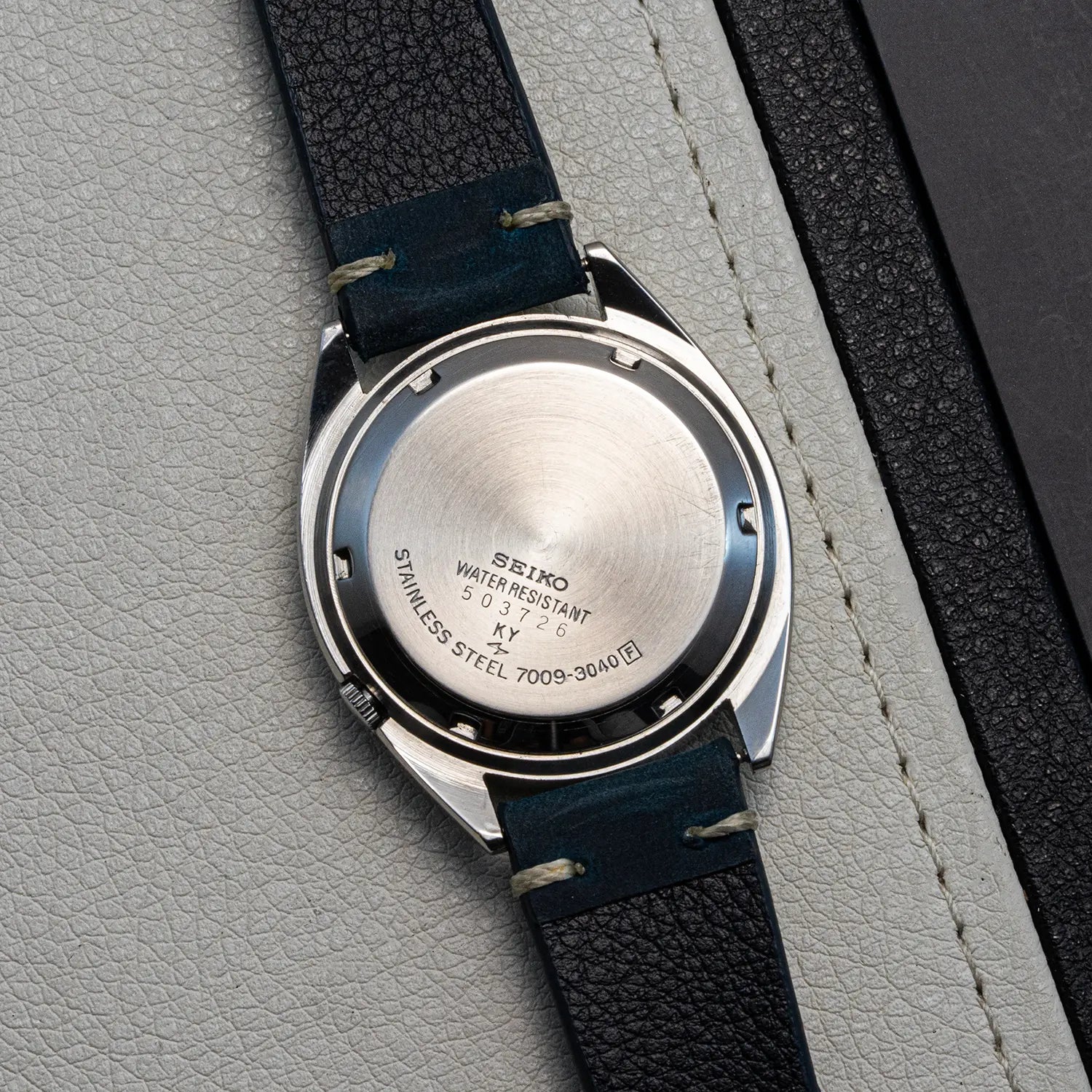 Close-up of a Seiko 5 7009 3040 backcase with a blue strap on a gray textured surface