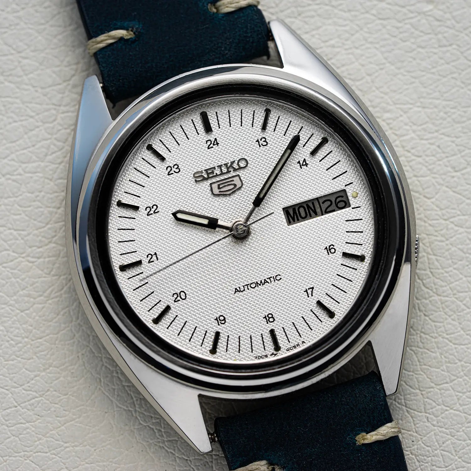 Seiko 5 7009 3040 with White Dial watch with a blue strap on a light gray background