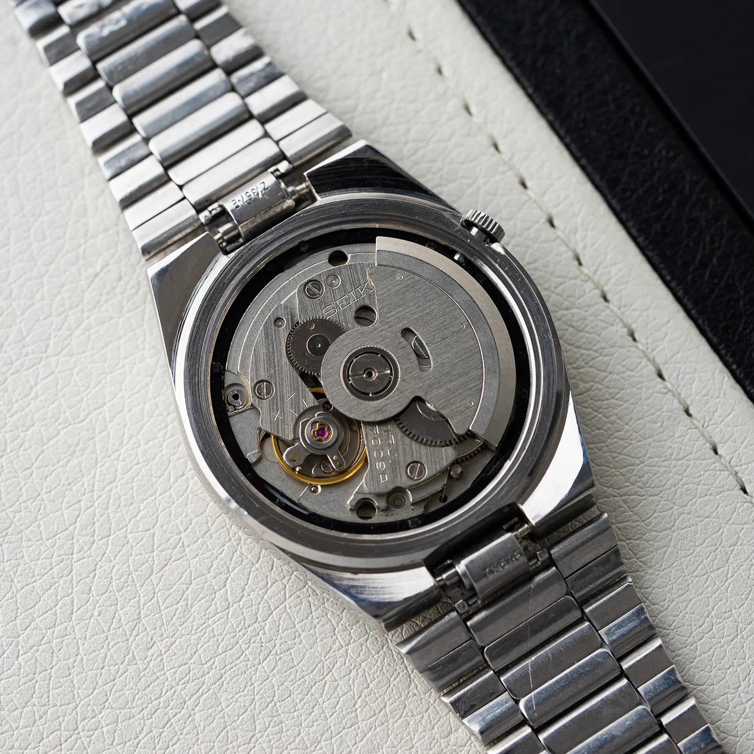 Close-up of a movement of Seiko 5, Ref. 7009-3130 with its back cover removed, revealing the mechanical components on a light gray background.