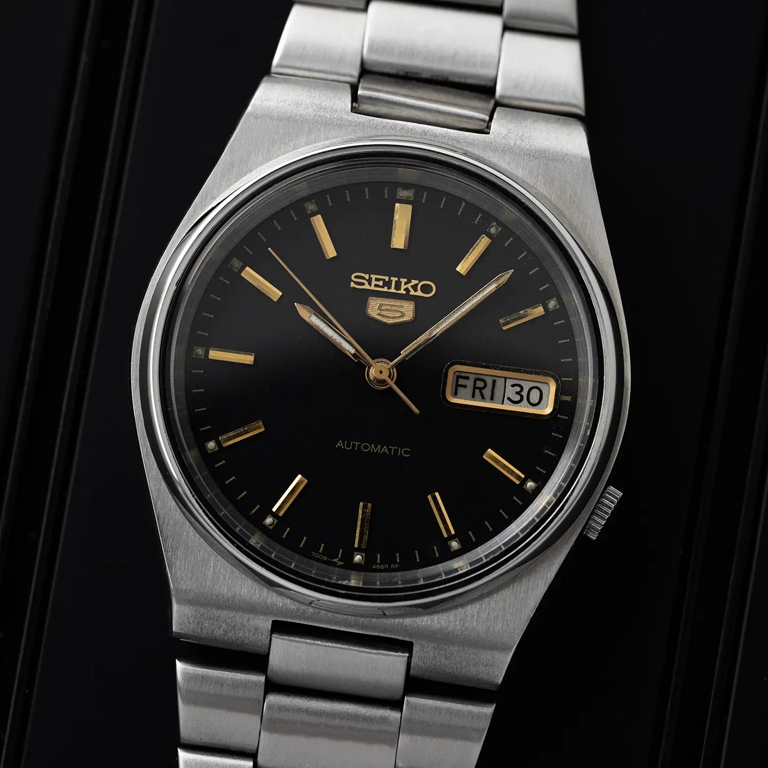 Seiko 5, Ref. 7009-3130 watch with black dial and silver metal strap on a dark background