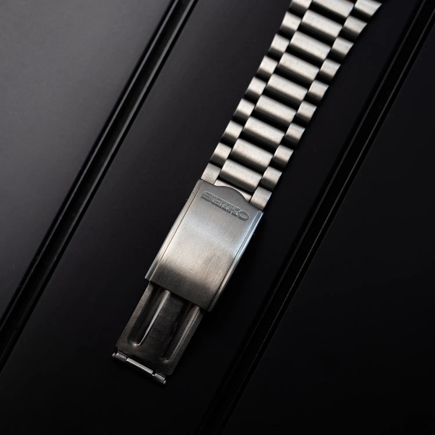 Metallic watch strap with Seiko clasp on a black background