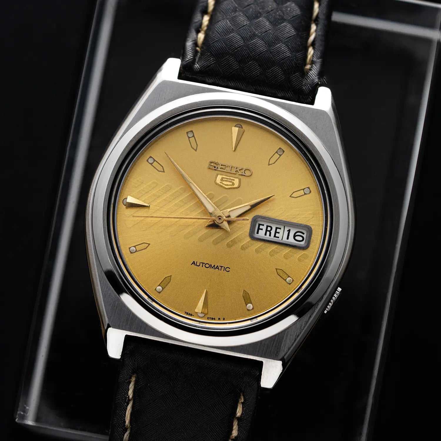 Seiko 5 7S26-8760 with gold face and black leather strap on a dark background