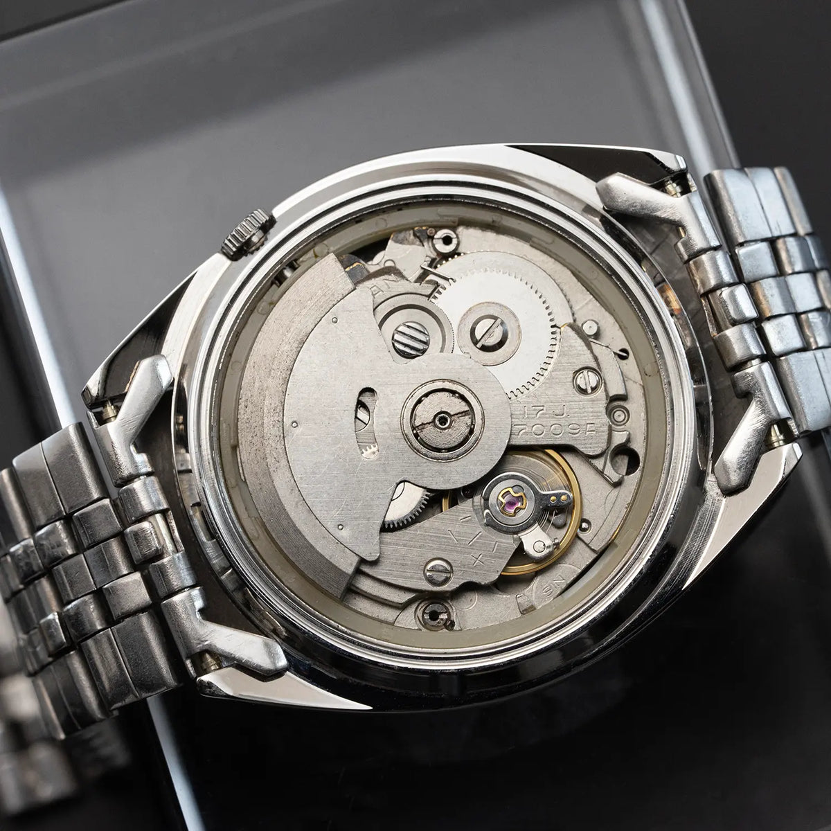Close-up of a silver watch with its back cover removed, revealing the mechanical components.