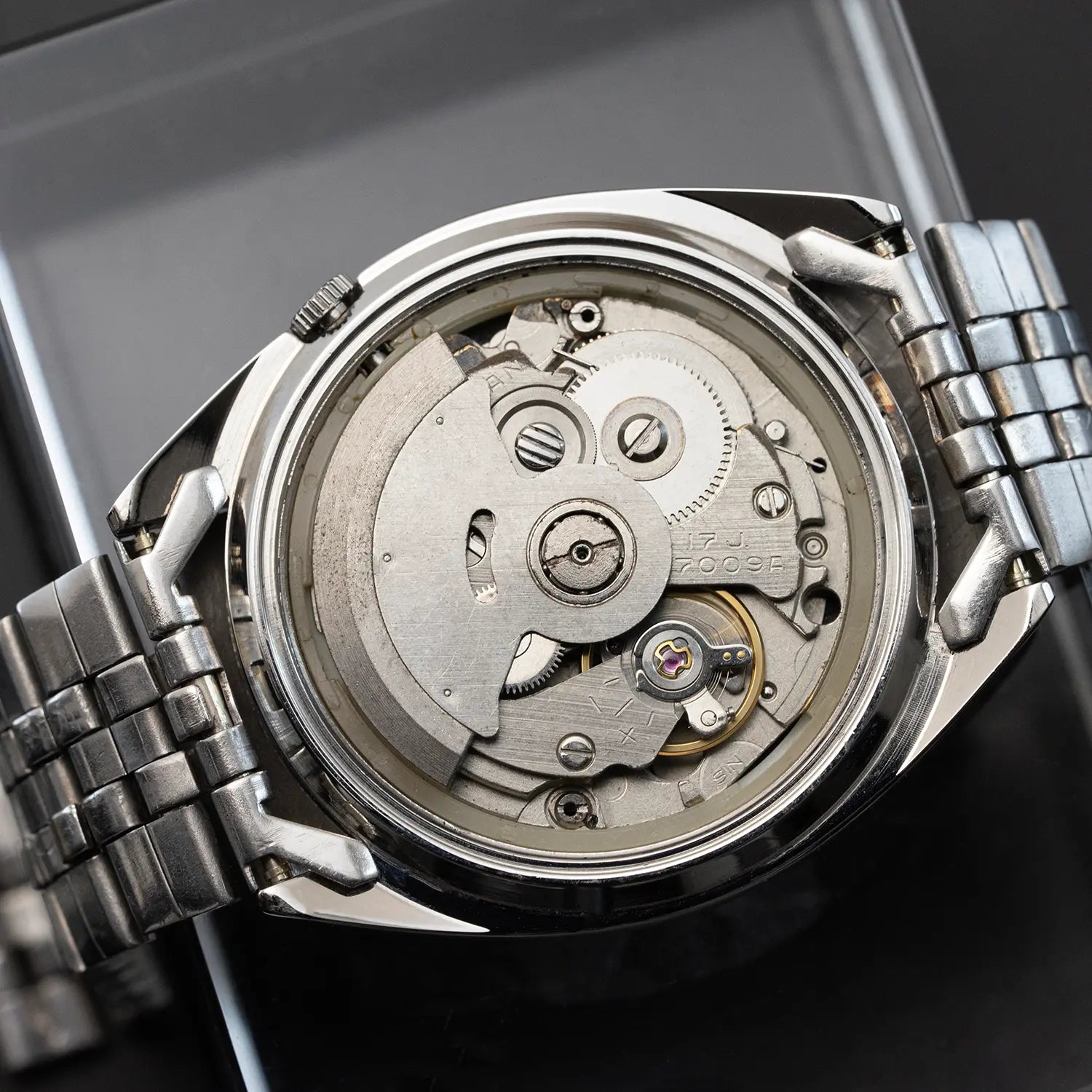 Close-up of a silver watch with its back cover removed, revealing the mechanical components.