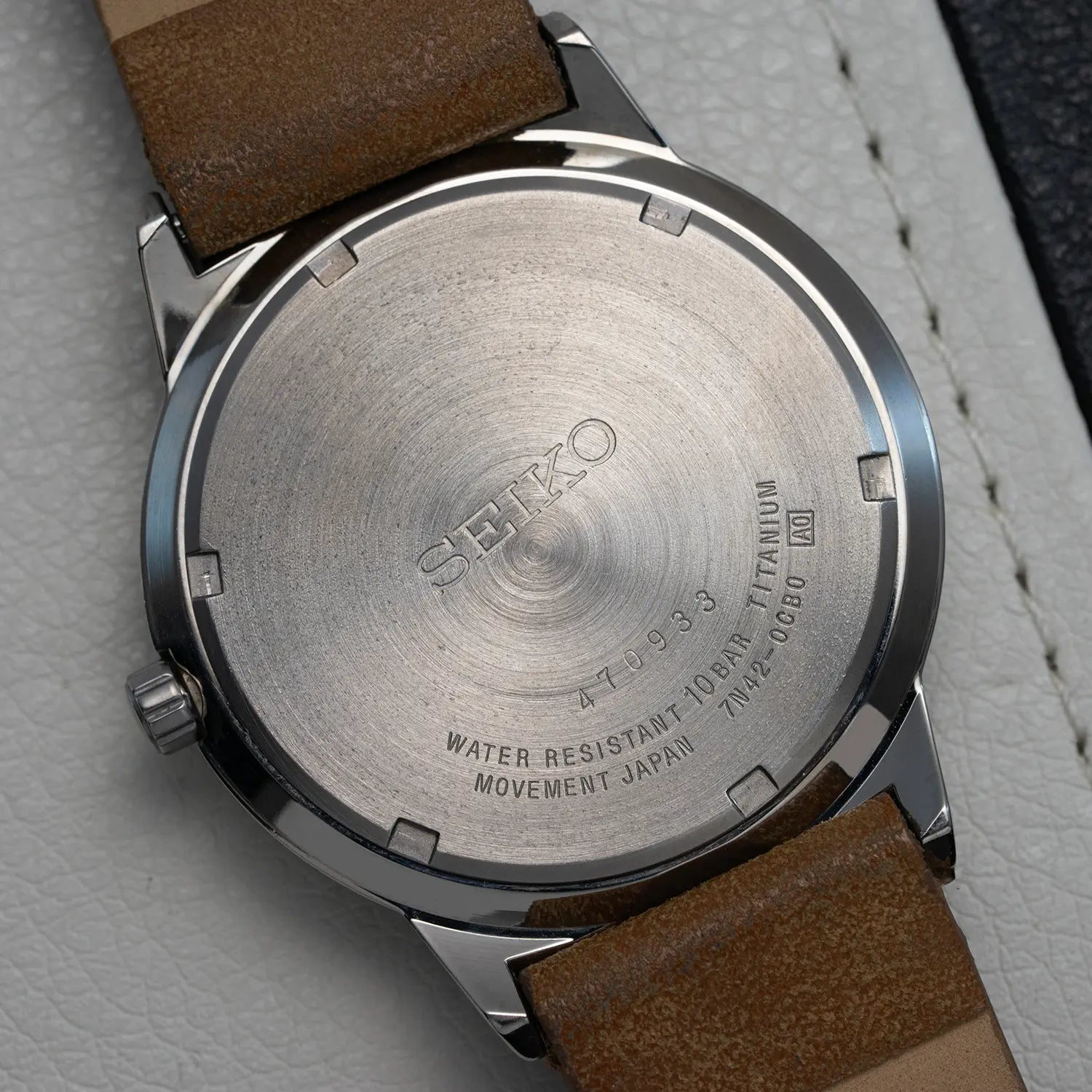 Seiko 7N42-0CB0 backcase with brown leather strap on a gray textured background
