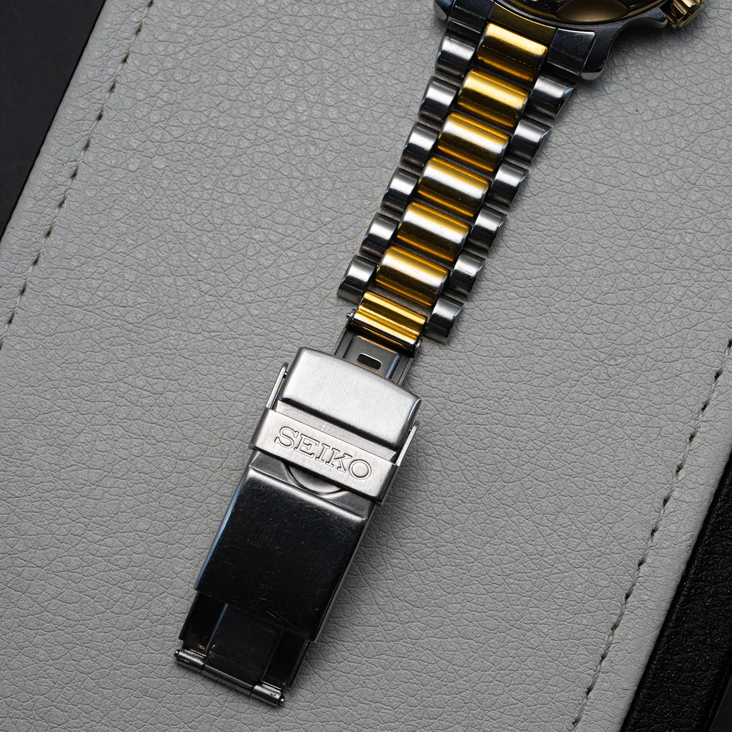 Close-up of a Seiko Scuba 200M, Ref. 5H25-6000 watch strap and buckle on a textured gray surface