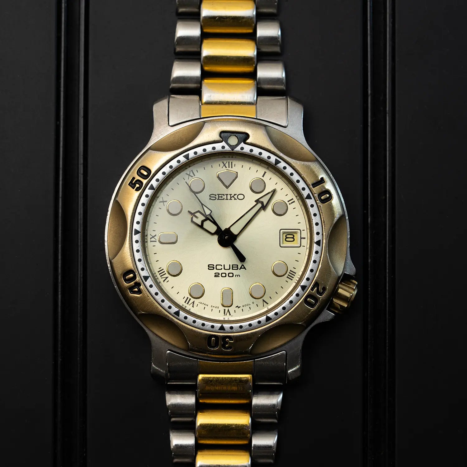 Seiko Scuba 200M, Ref. 5H25-6000 top view on watch with gold and silver band on a black background
