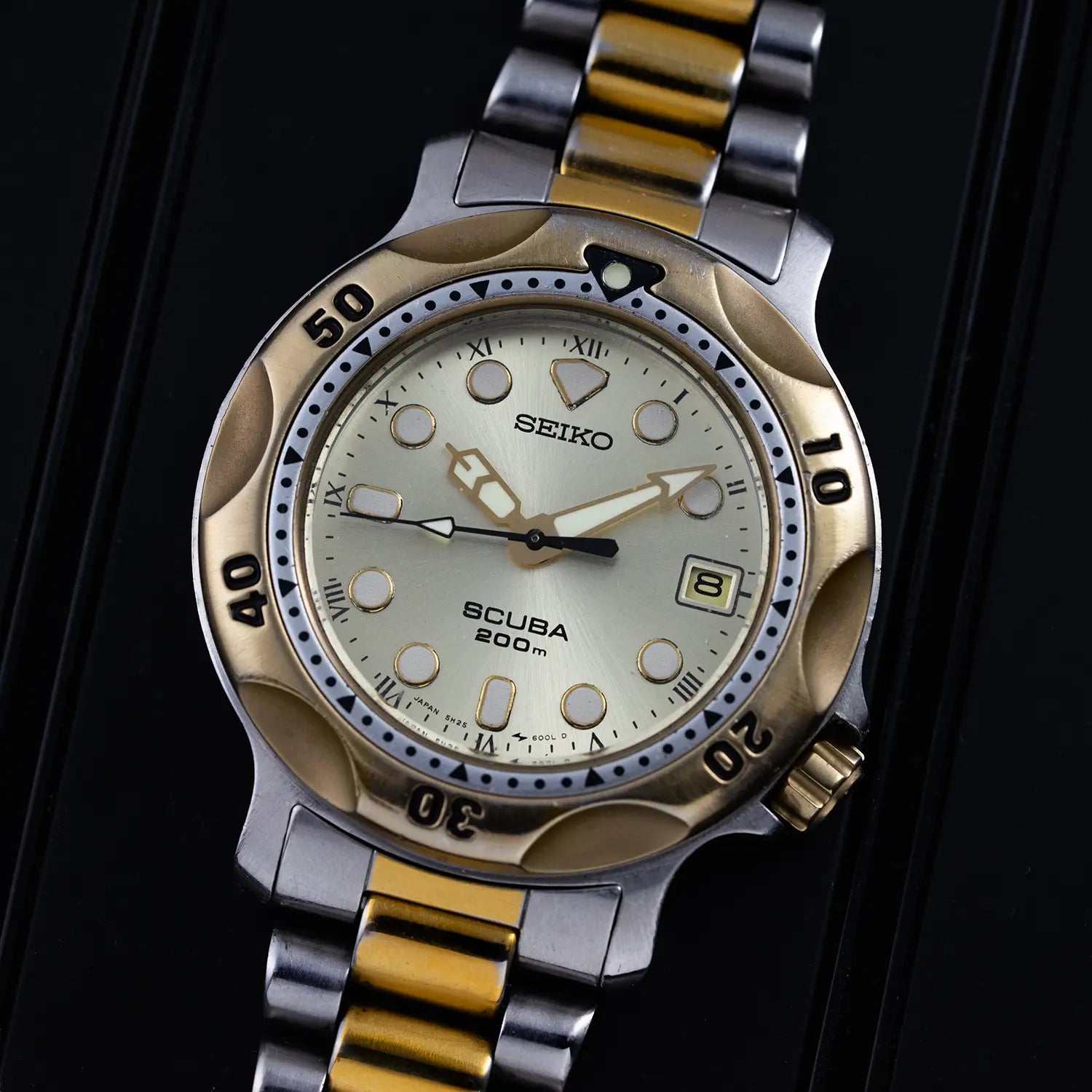 Seiko Scuba 200M, Ref. 5H25-6000 watch with gold and silver band on a black background