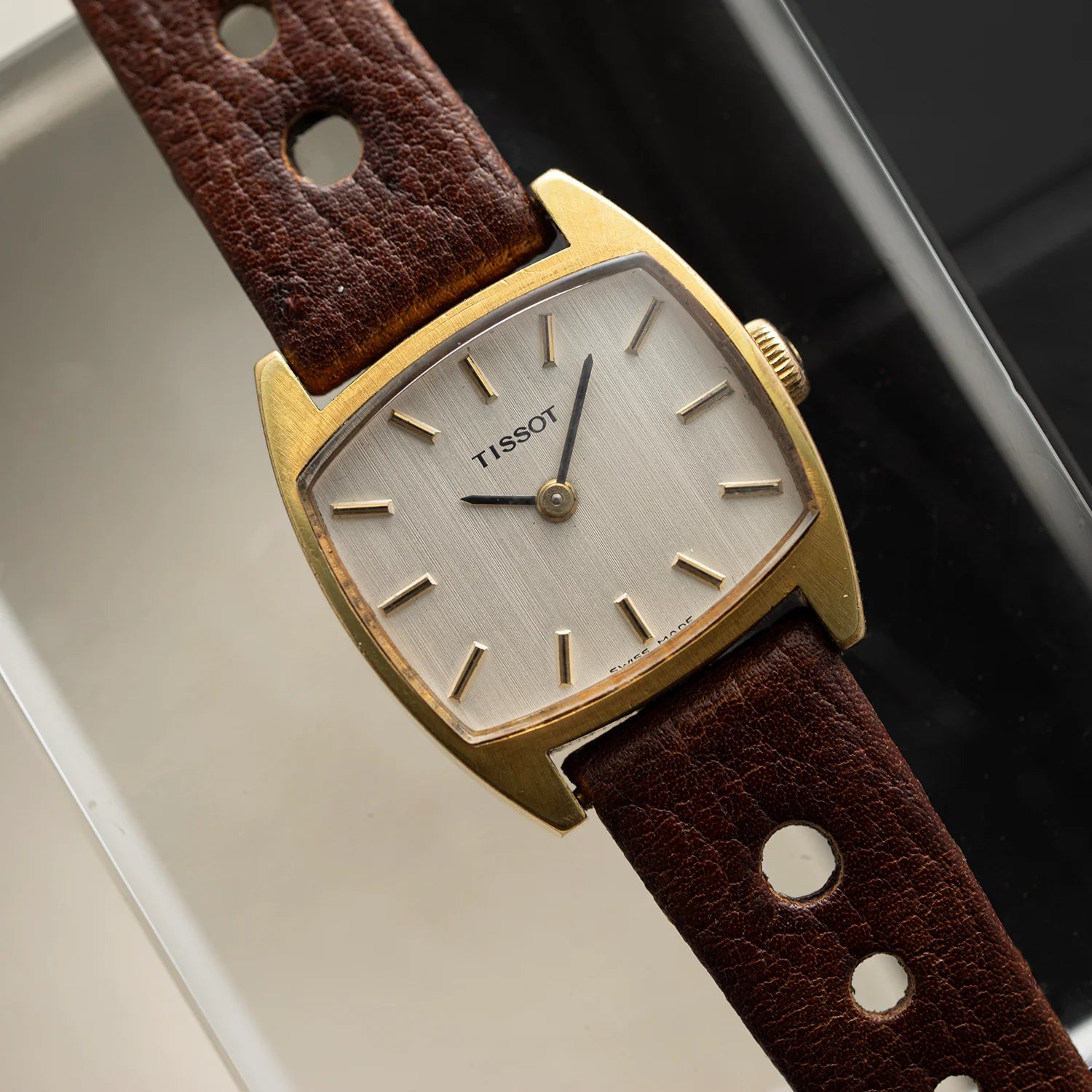 Tissot vintage women’s dress watch from 1978 with gold plated tonneau-shaped case, silver dial, and brown leather strap, close-up top view