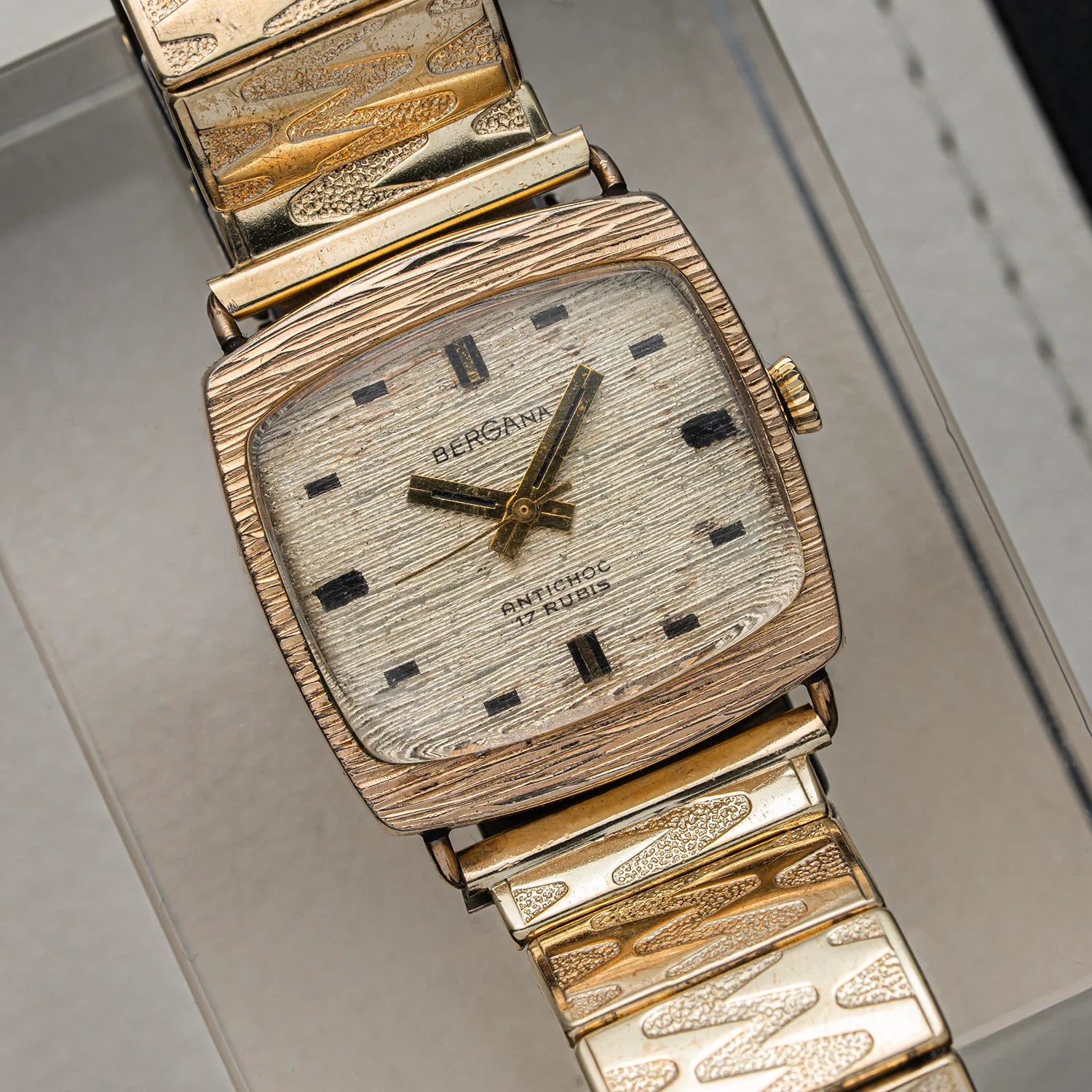 A vintage Bergana PUW 460 watch with a textured gold-tone case and a matching textured gold-tone link bracelet, resting on a light gray surface.