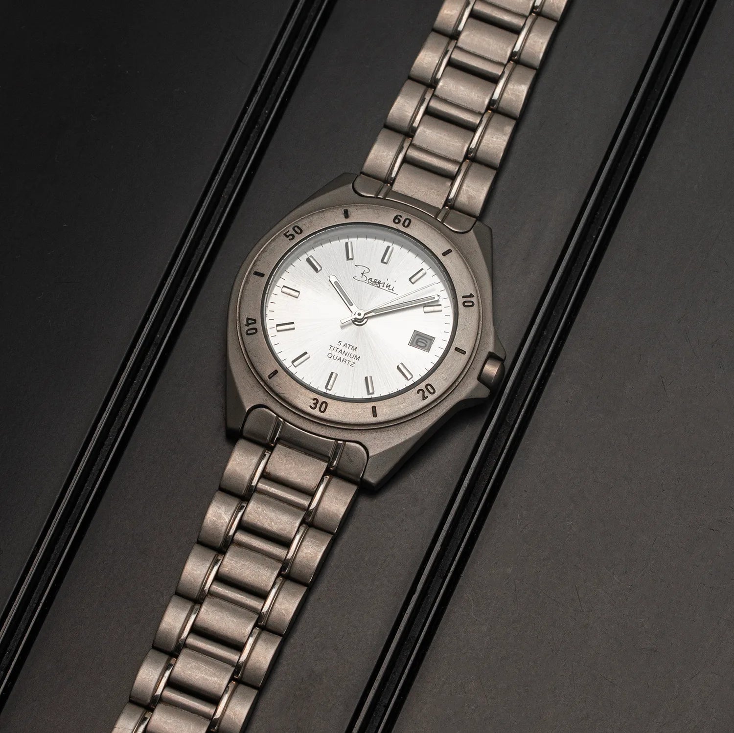 A Bossini Titanium watch with a silver-toned and link bracelet, featuring a white dial with black markings and a date window.