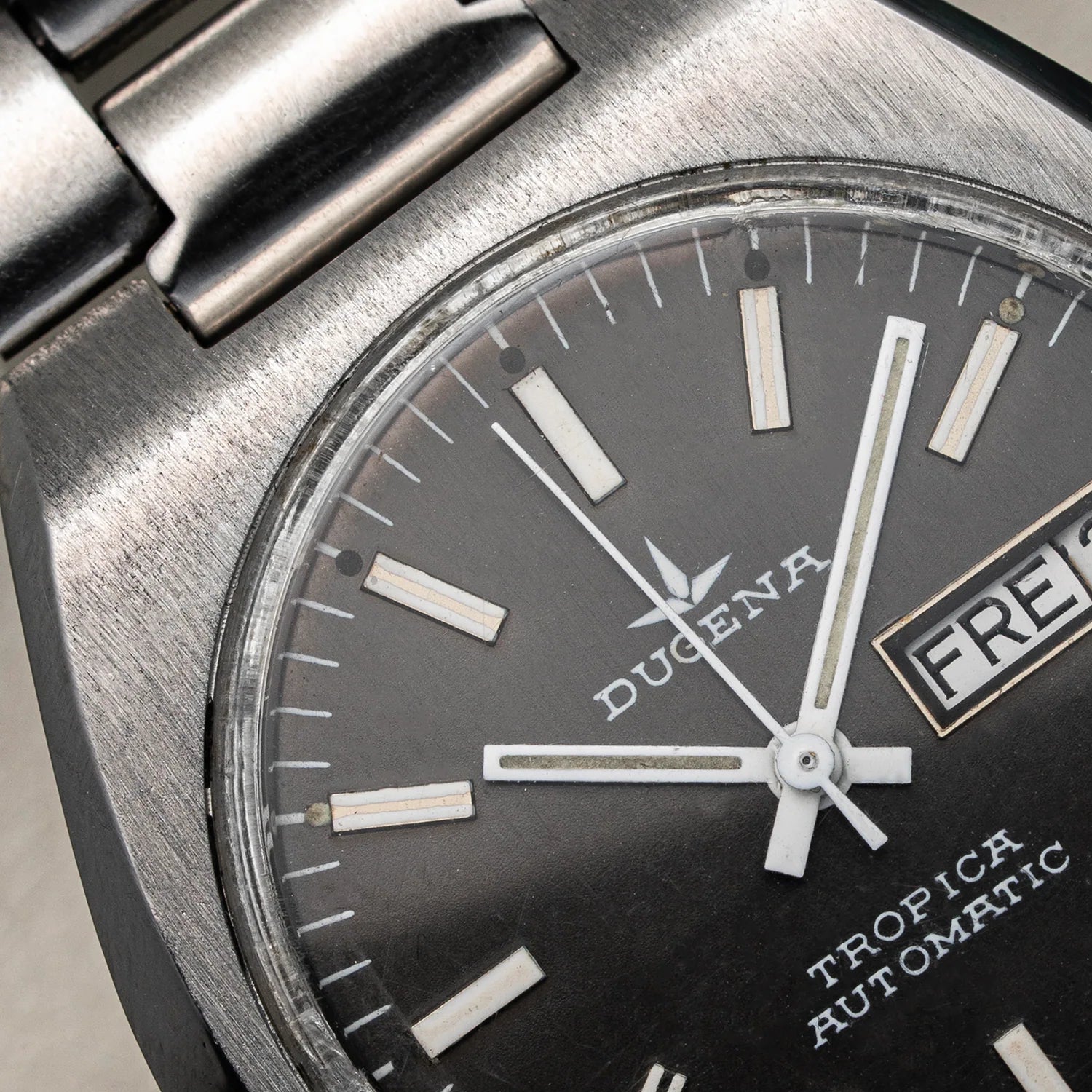Close-up of a Dugena Tropica Automatic watch with a brushed stainless steel case, black dial, silver hour markers, and a day-date window.