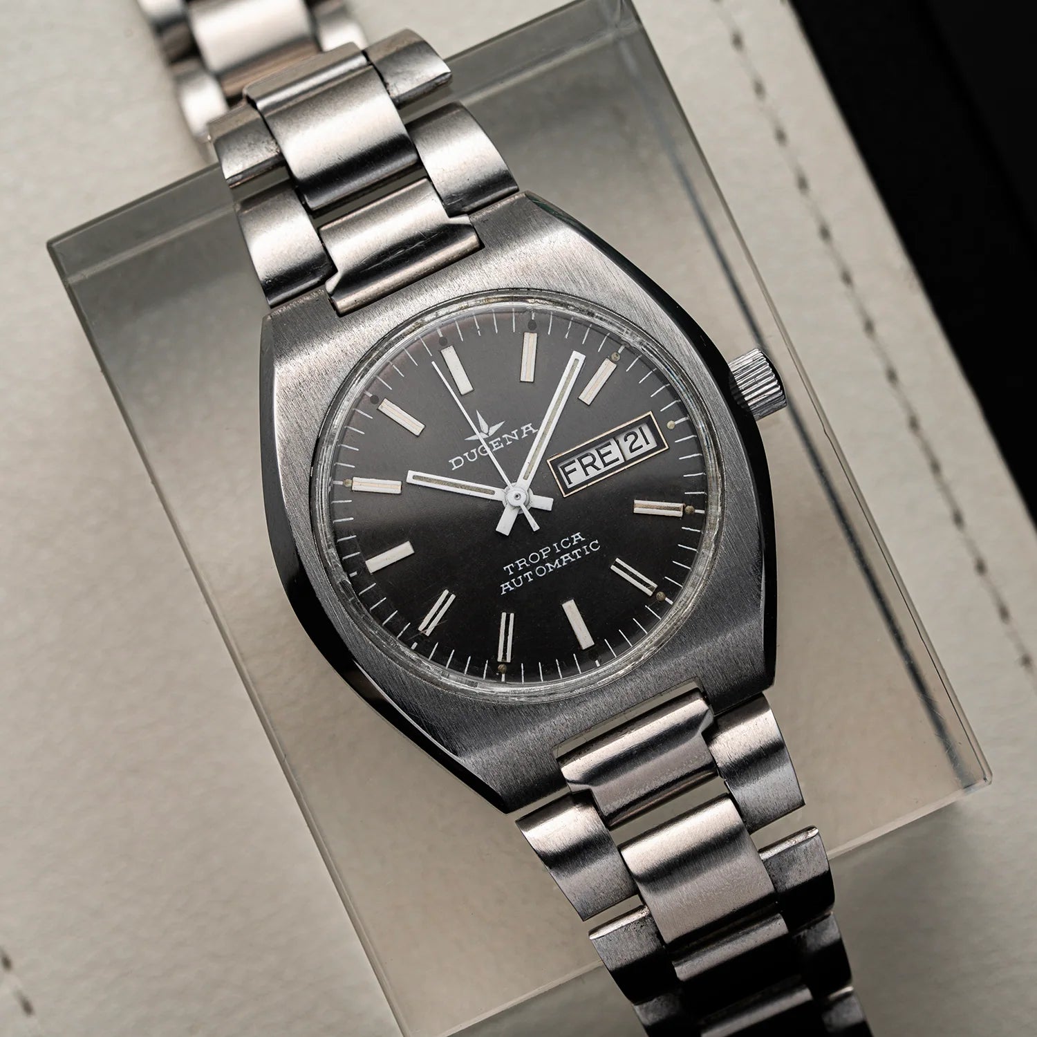 A Dugena Tropica Automatic wristwatch with a brushed silver-tone metal case and bracelet, featuring a black dial with white indices and a day/date window.