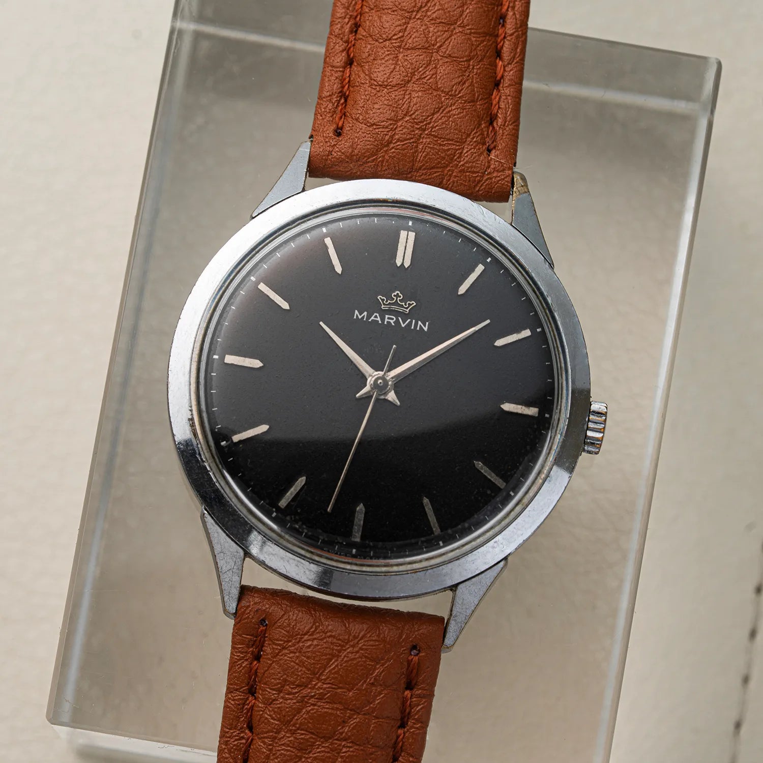A vintage Marvin Cal. 560 wristwatch with a black dial, silver-tone case, and brown leather strap, displayed on a clear acrylic stand.