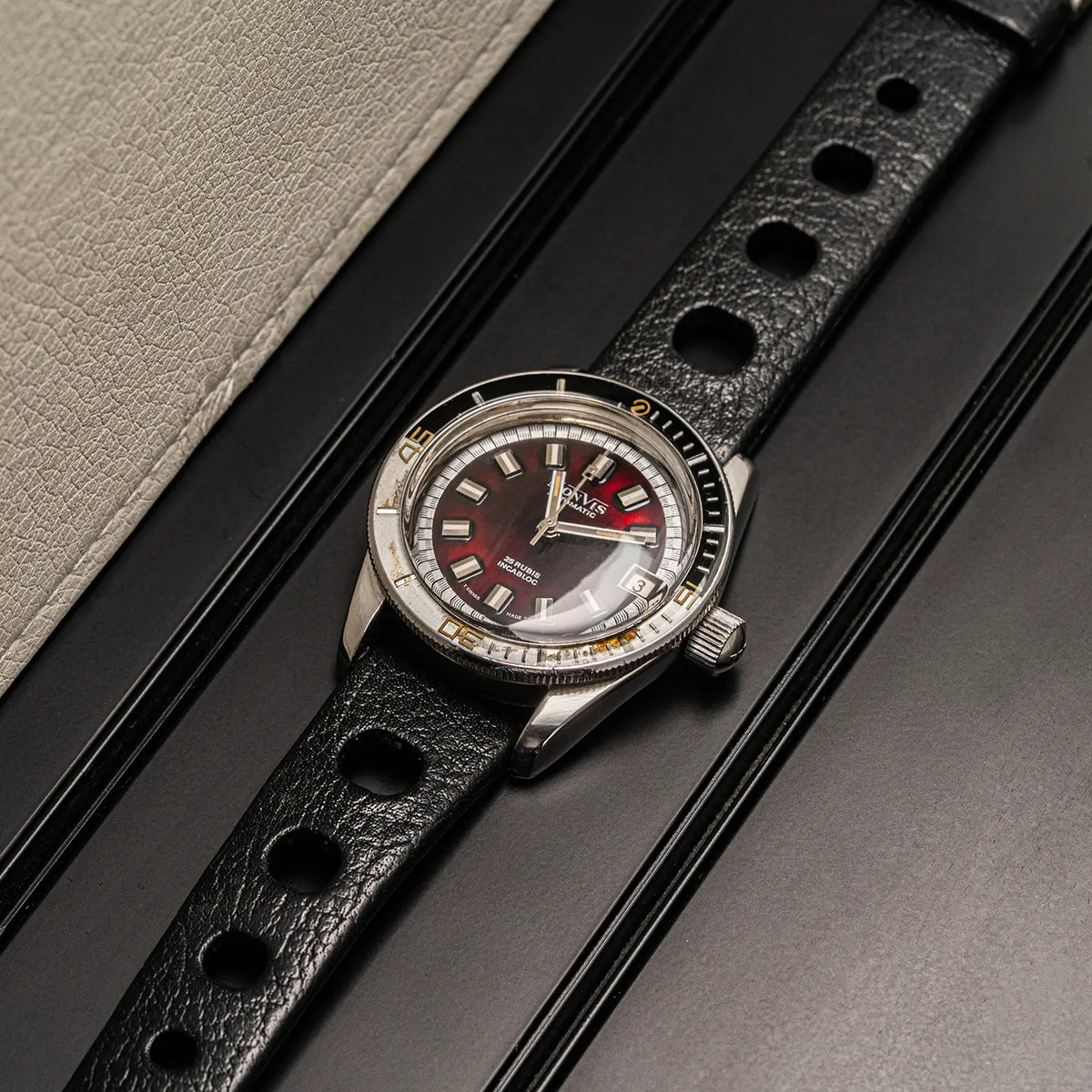 A wristwatch Monvis Bakelite Diver, 20 ATM, Ref. 1.18, Cal. ETA 2783, Men’s Diving with a black textured strap and a dark dial, photographed diagonally on a black surface with a light beige textured panel in the background.