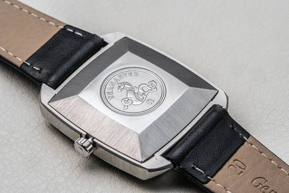 Close-up of the back of a wristwatch with a brushed silver-tone case and a dark leather strap on a light textured surface. The case is engraved with a circular emblem featuring a horse and the text 'SILVERSTED'.
