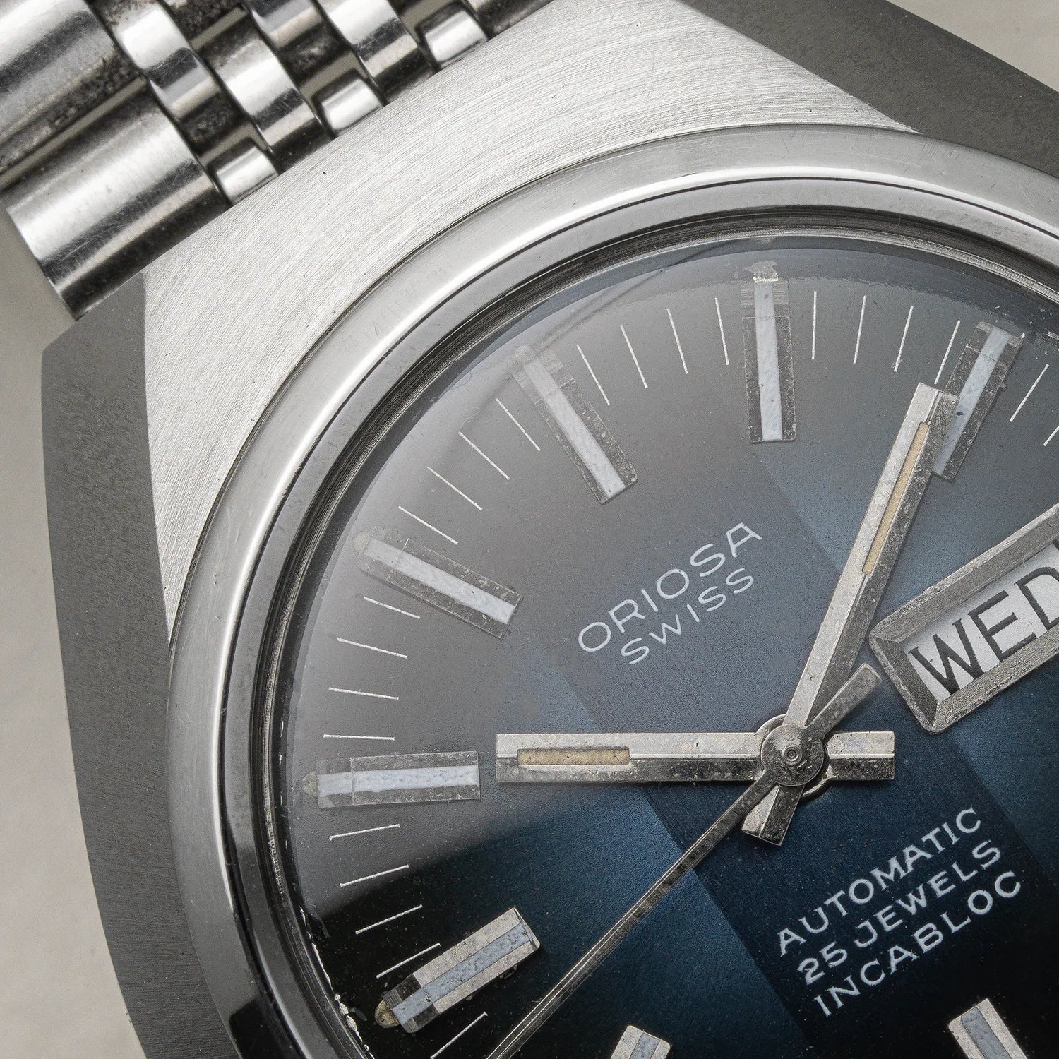 Close-up of an Oriosa, ETA 2789 Swiss Automatic 25 Jewels Incabloc watch featuring a brushed silver-tone stainless steel case, a dark blue sunburst dial, and a matching steel bracelet.