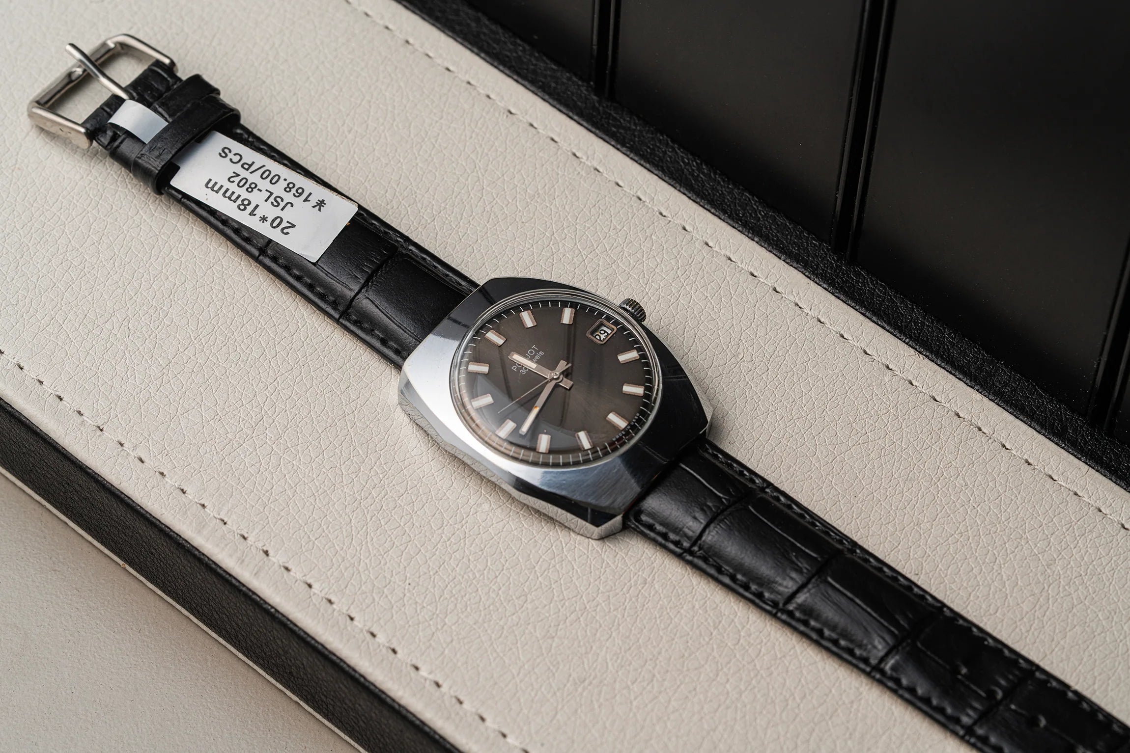 A vintage-style wristwatch Poljot 30 Jewels with a dark brown dial and a black leather strap, resting diagonally on a cream-colored textured surface with a black background.